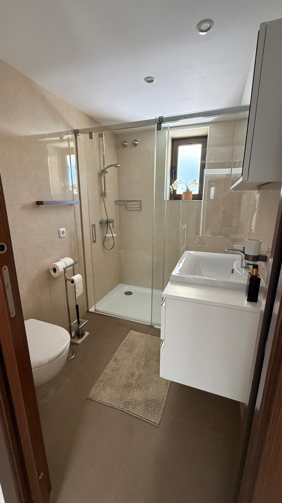 Modern bathroom featuring a glass shower, sink, and light tiles.