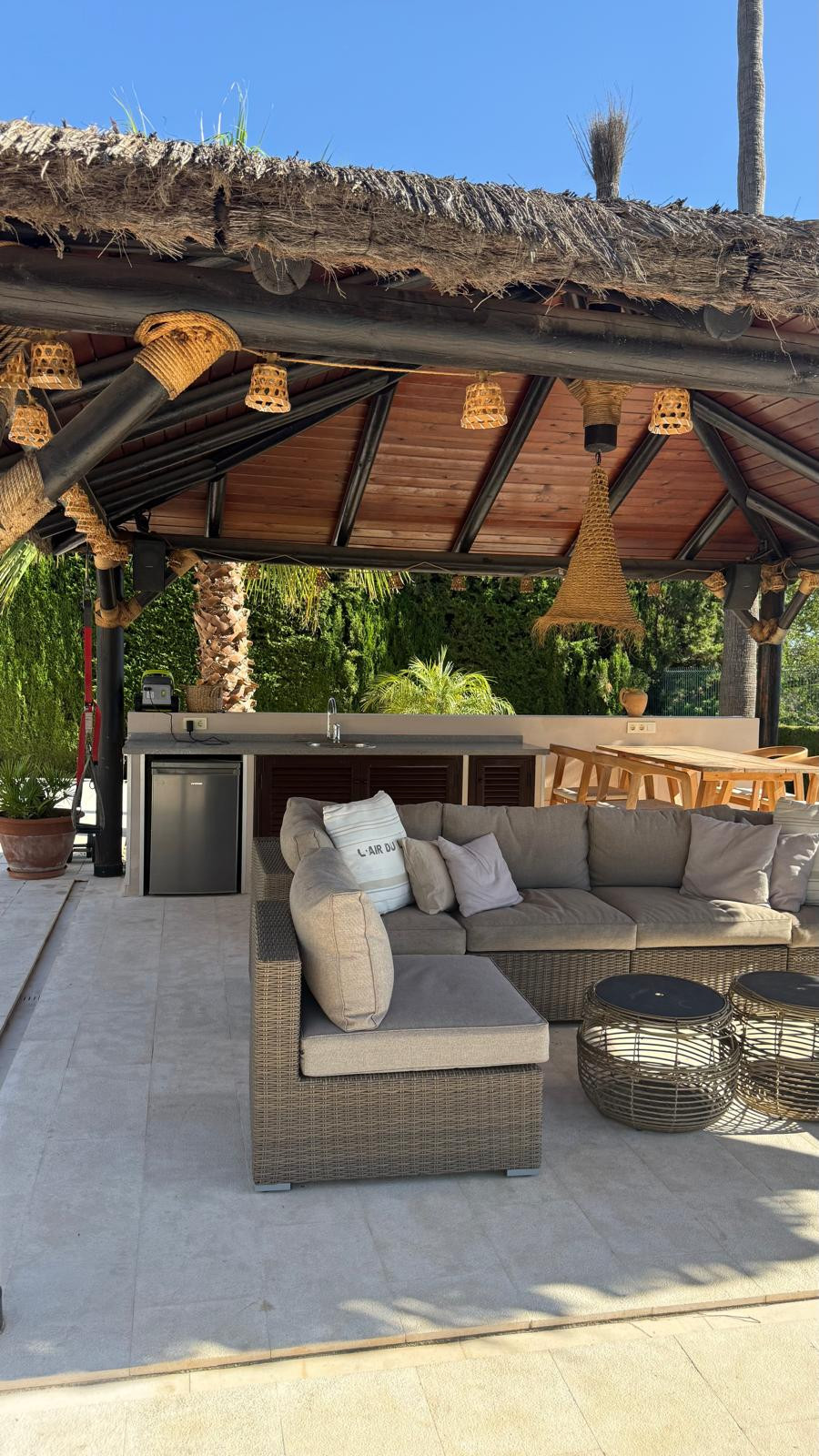 Outdoor kitchen area under a thatched roof with seating and a bar.