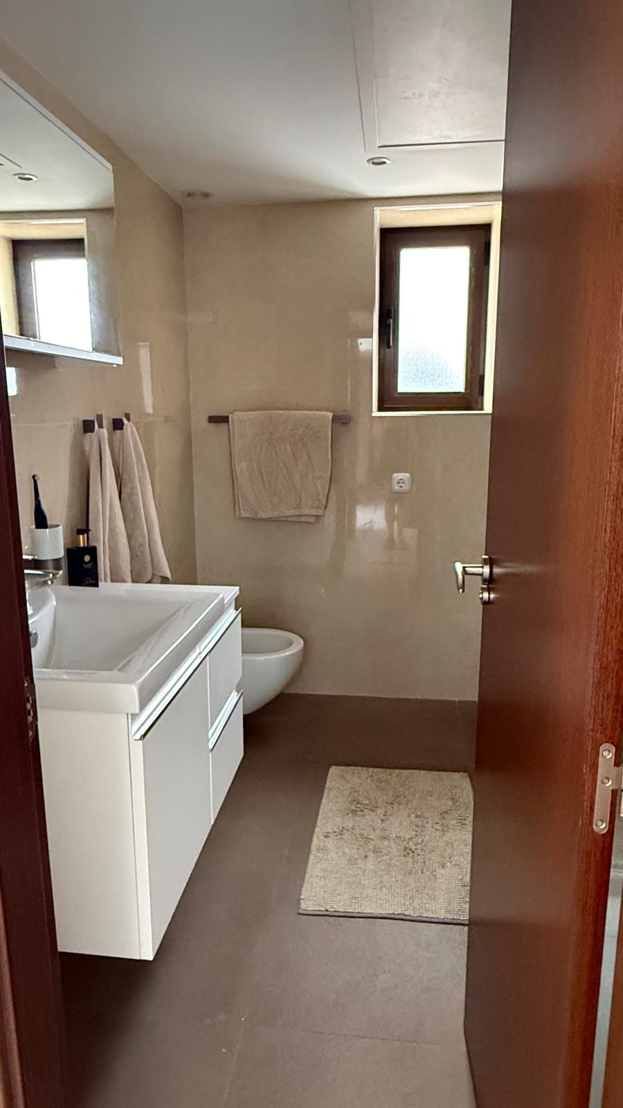 Bathroom with neutral tiles, vanity sink, bidet, and window with natural light.