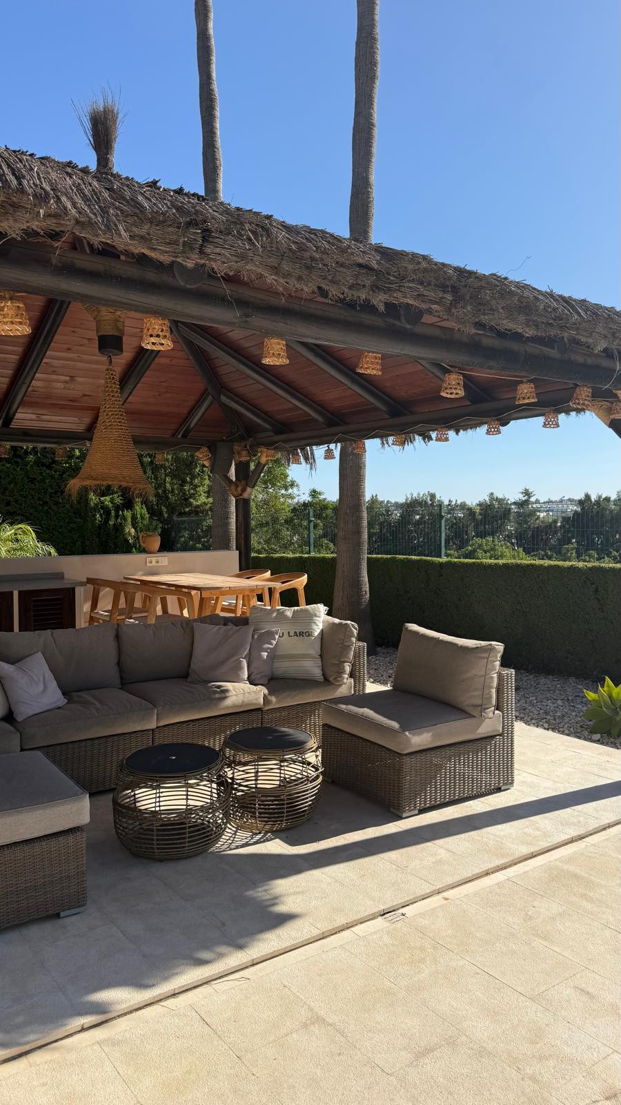 Seating area with a view of the garden and outdoor dining space beneath a roof.