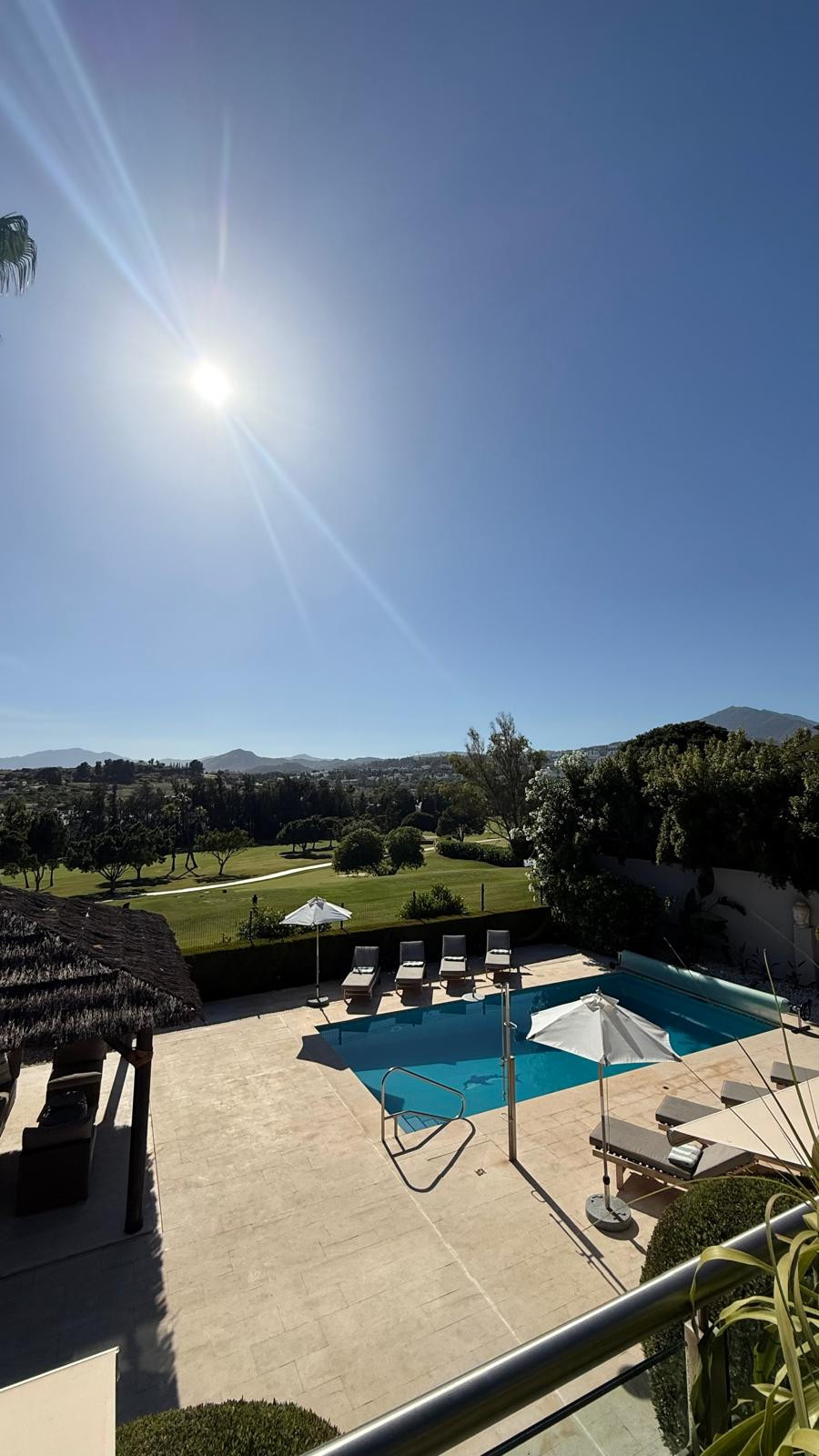 Outdoor pool area with loungers and umbrellas, set against a clear blue sky and landscape.