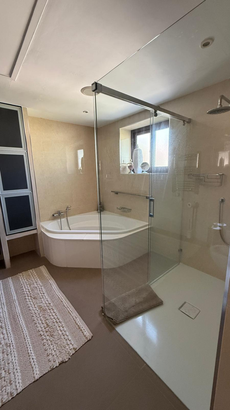 Stylish bathroom with a glass shower, corner bathtub, and natural light from a nearby window.