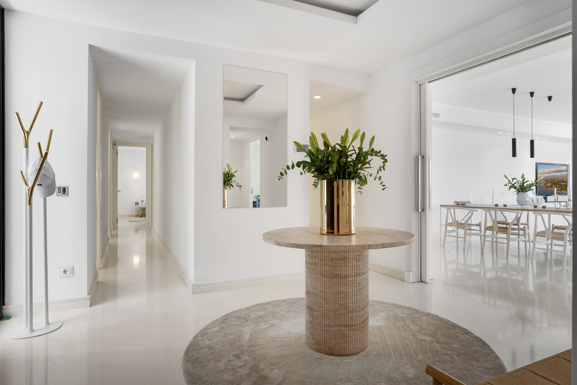 Entryway featuring a round table with plants and a mirror, bright walls, and minimalist decor.