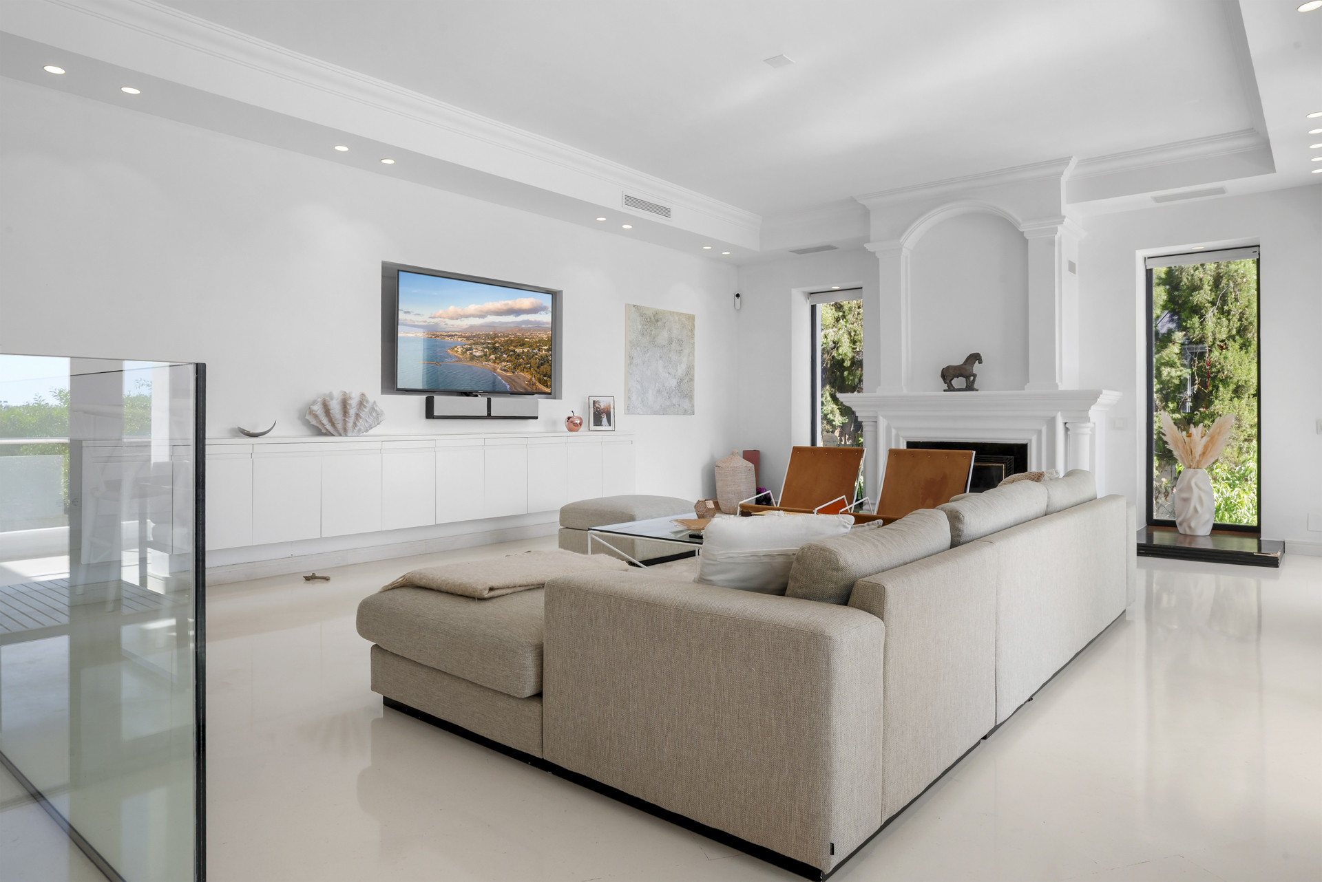 Living room showcasing a sectional sofa with a TV mounted on the wall and a fireplace, and large windows.