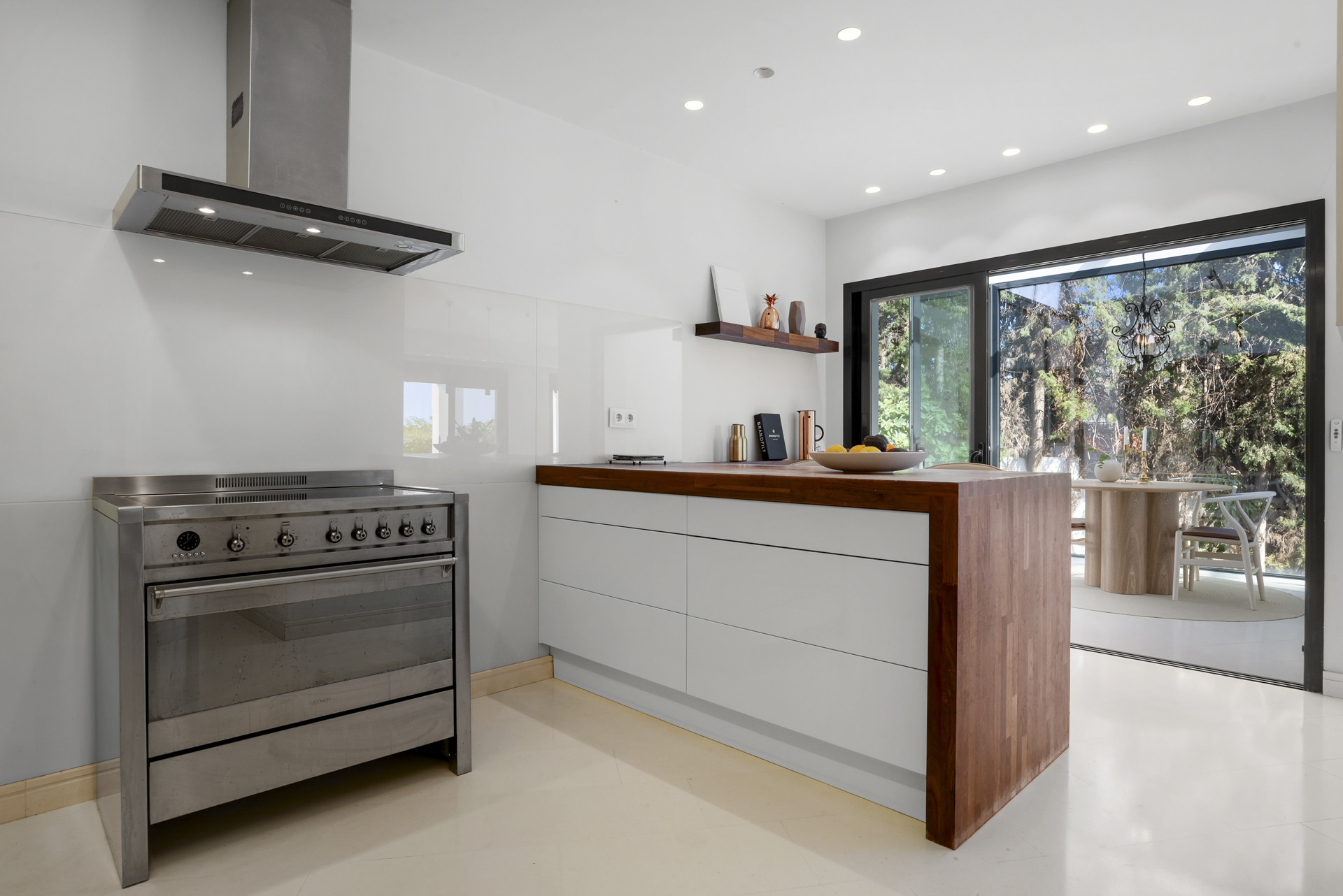 Modern kitchen with stainless steel appliances and a wooden island, opening to an outdoor view.
