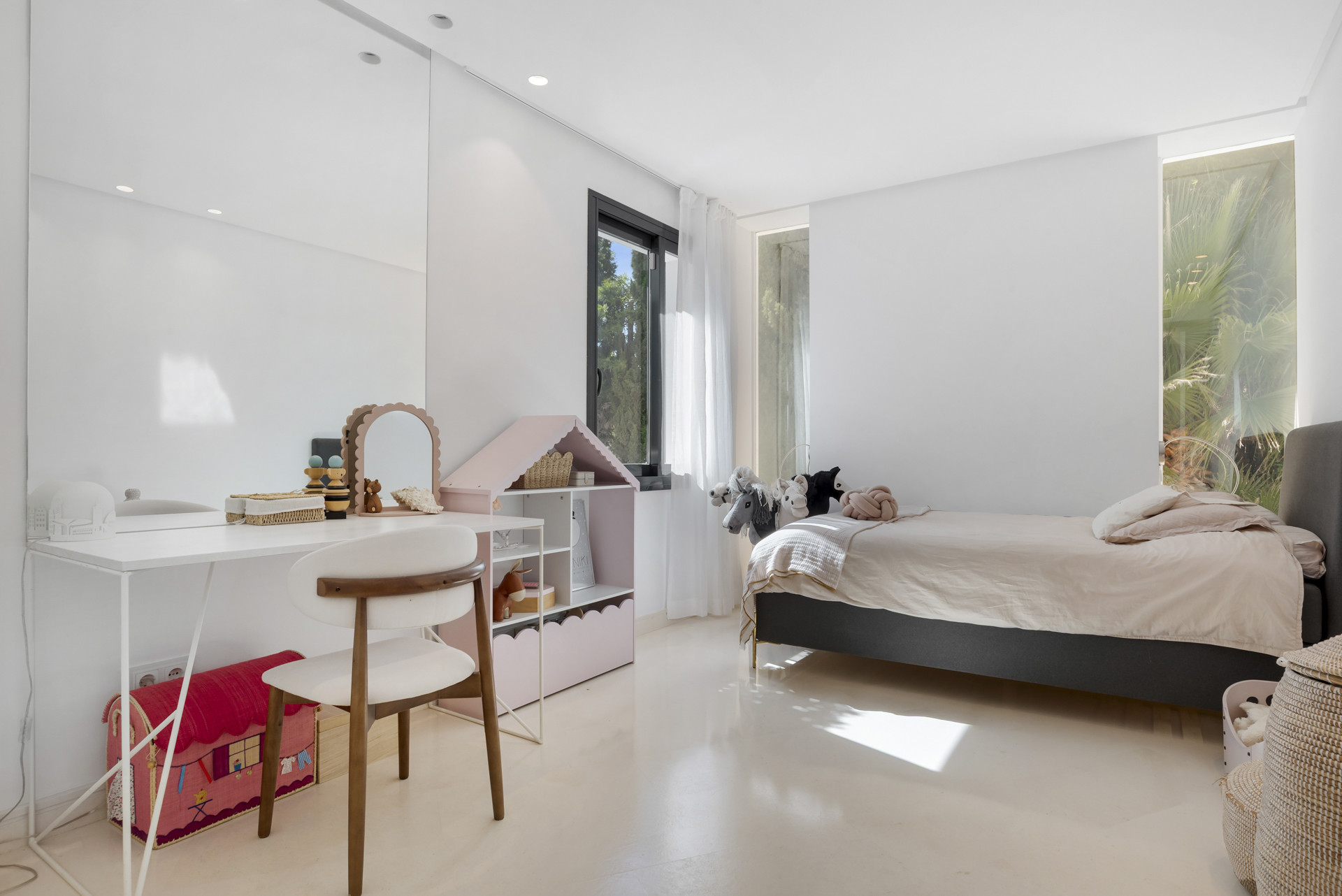 Children's bedroom featuring a bed, a mirror, a desk, and a playhouse beside the window.