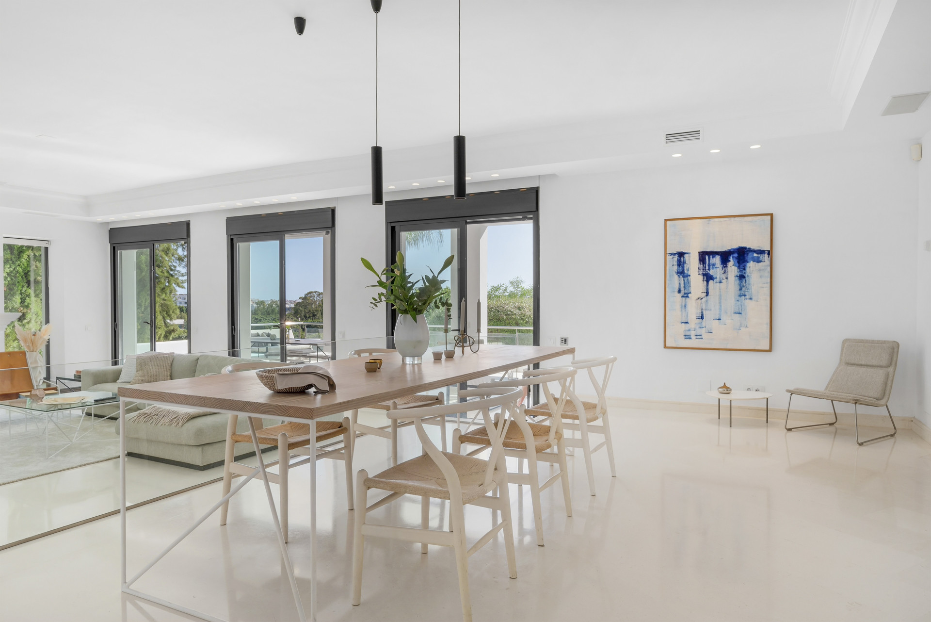 Dining area with a long wooden table, modern chairs, and large windows letting in natural light.