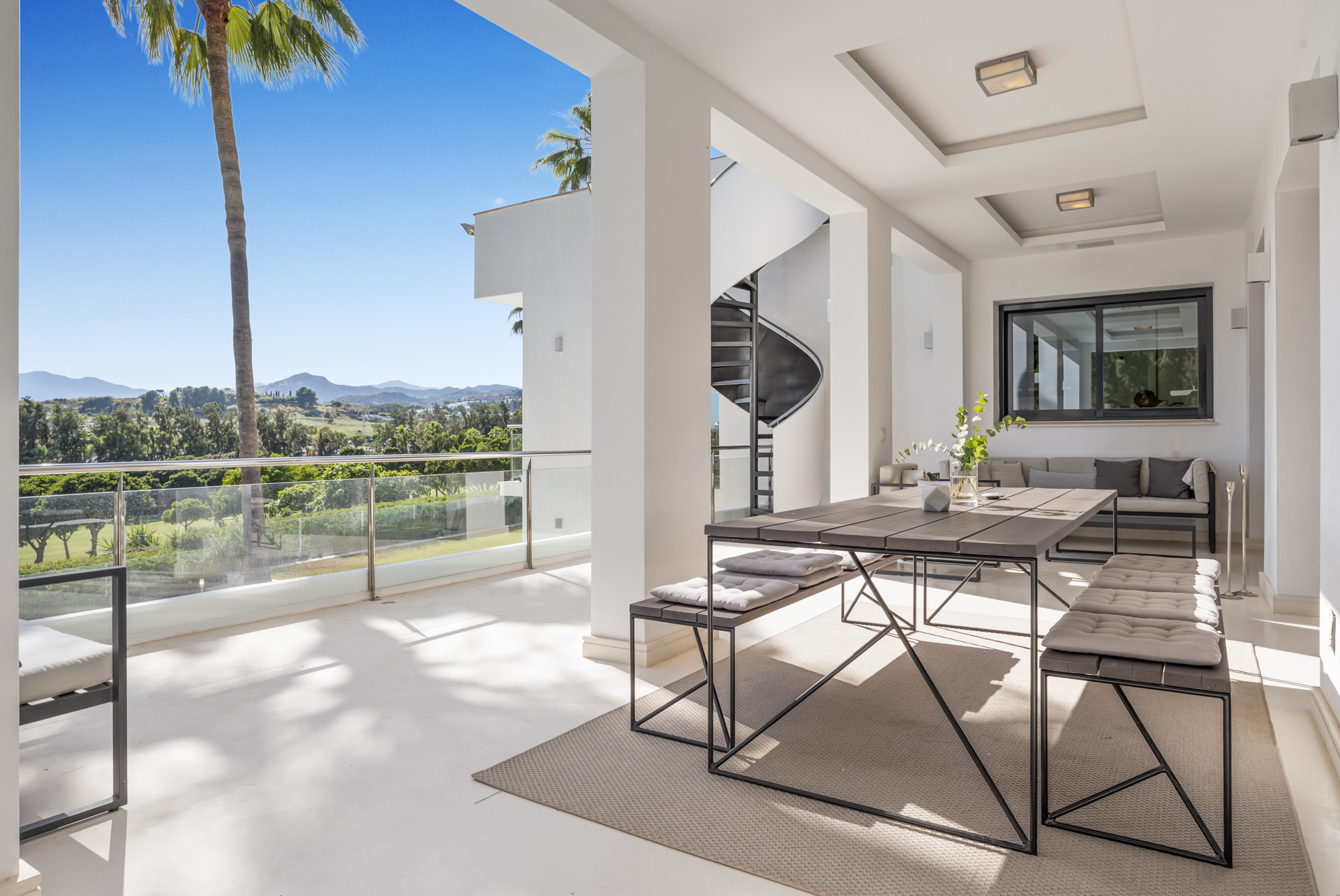 Dining area on terrace featuring a large table, seating and a view of distant mountains and palm trees.