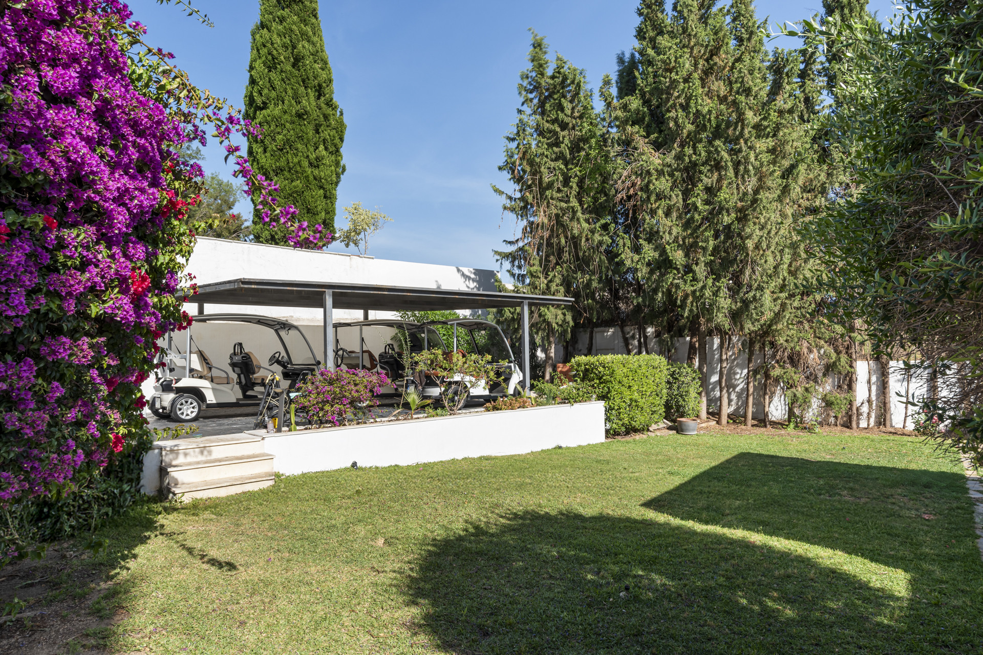 Garden area with golf carts under a canopy and blooming flowers.