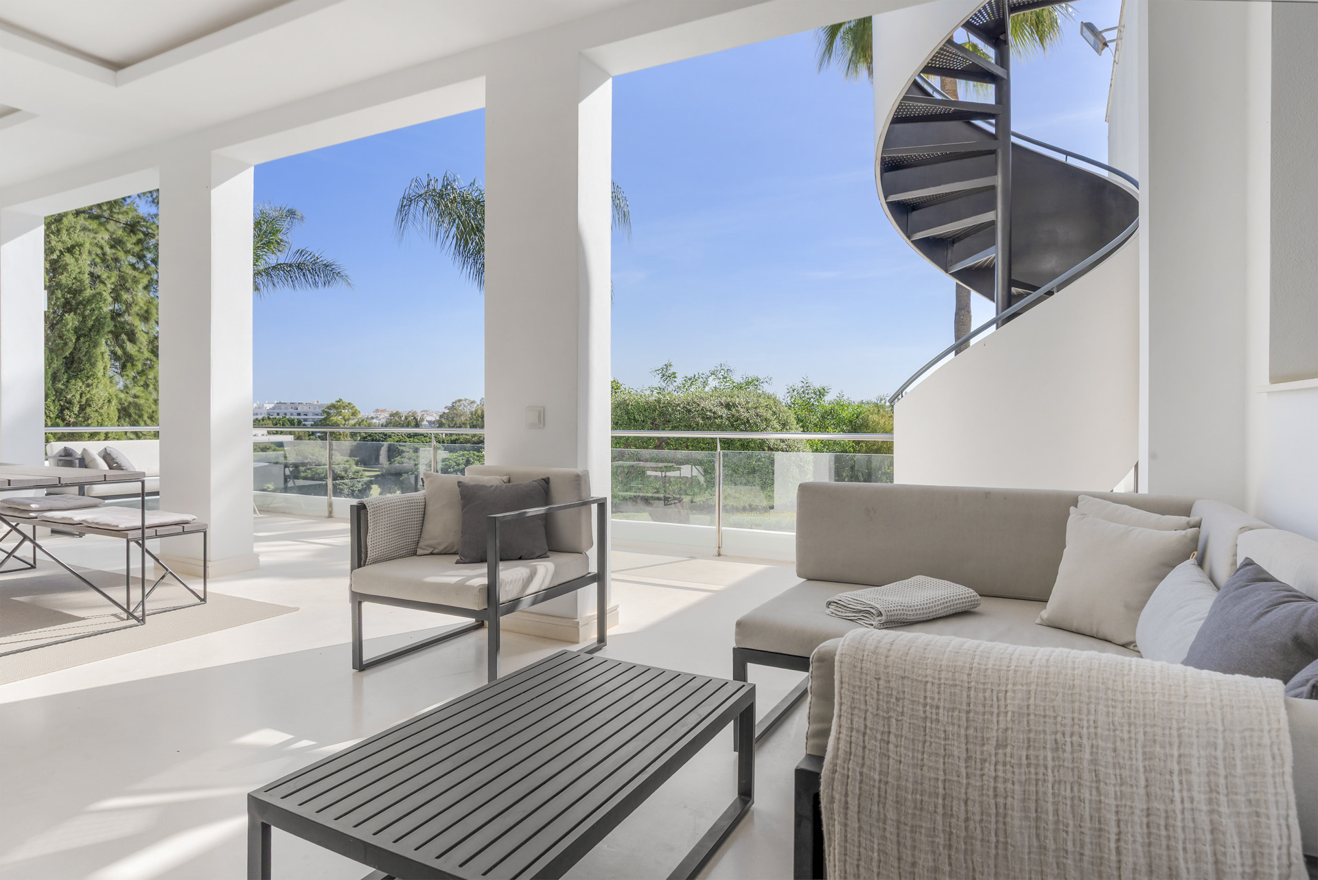 Spacious terrace with seating area, large spiral staircase, and views of surrounding greenery and blue sky.