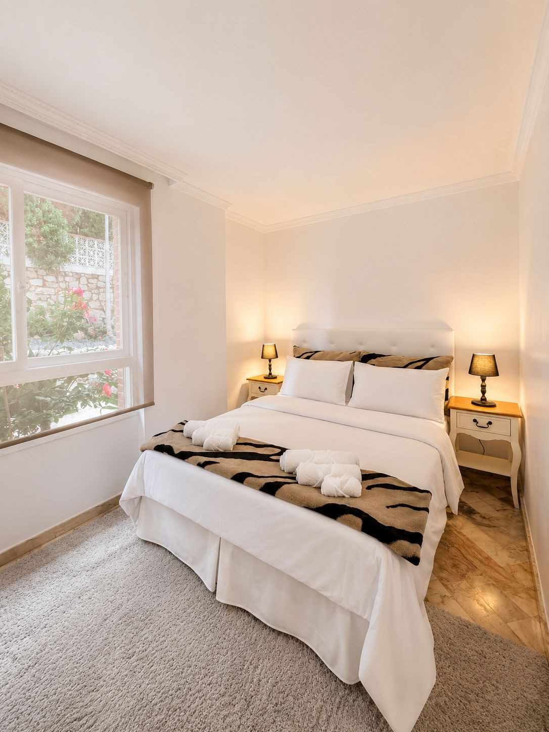 Cozy bedroom with a double bed, patterned throw, and window with greenery outside.