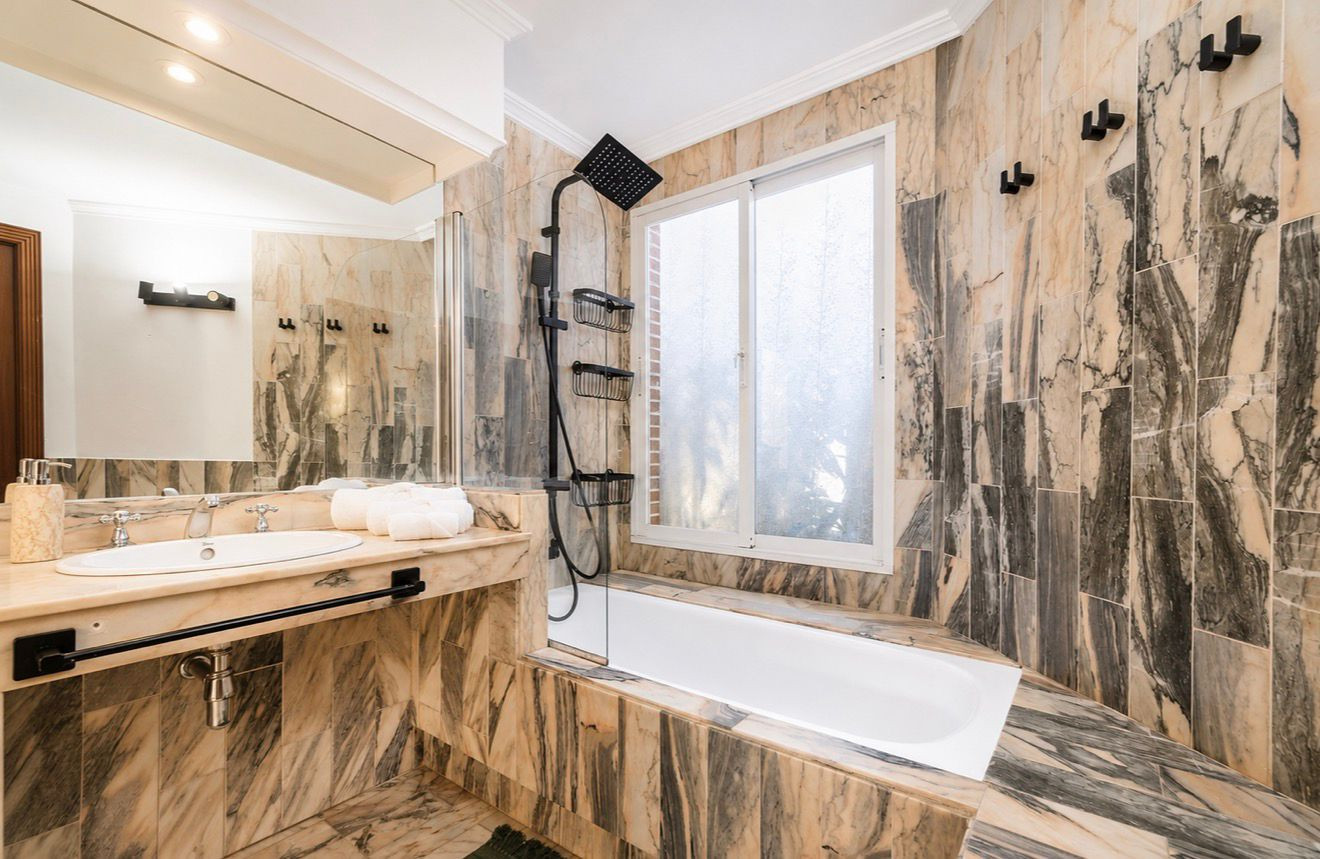 Marble-clad bathroom featuring shower and bathtub with natural light.