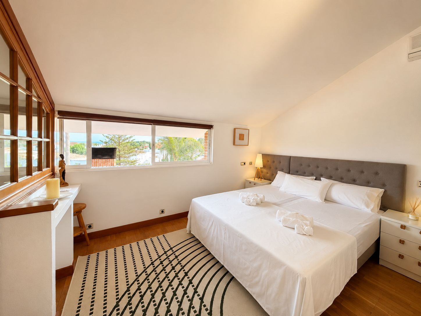 Bright bedroom featuring a large bed, wooden accents, and a window with a view.