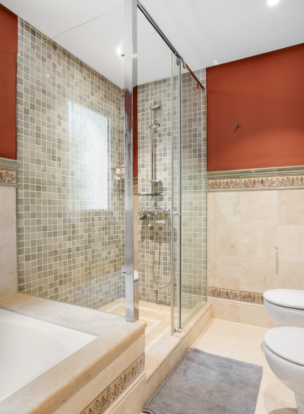 Shower area with a glass enclosure, modern fixtures, and mosaic tile design.
