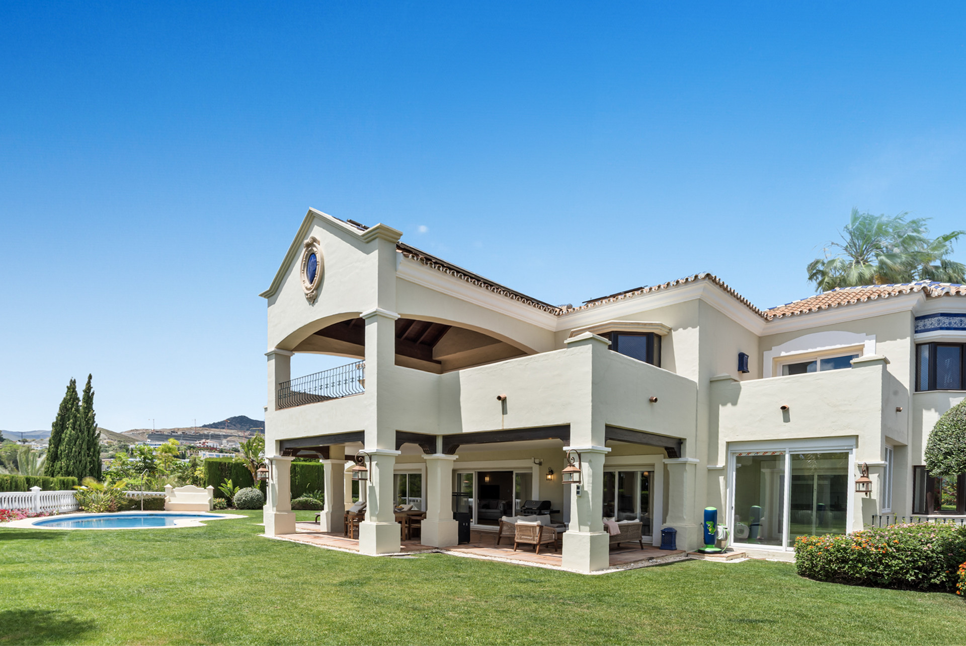 Exterior view of the house showcasing gardens and pool, with a clear blue sky.
