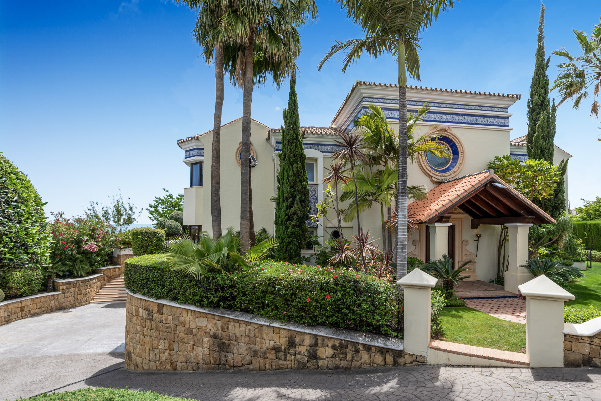 Exterior view of the house featuring palm trees and colorful plants.
