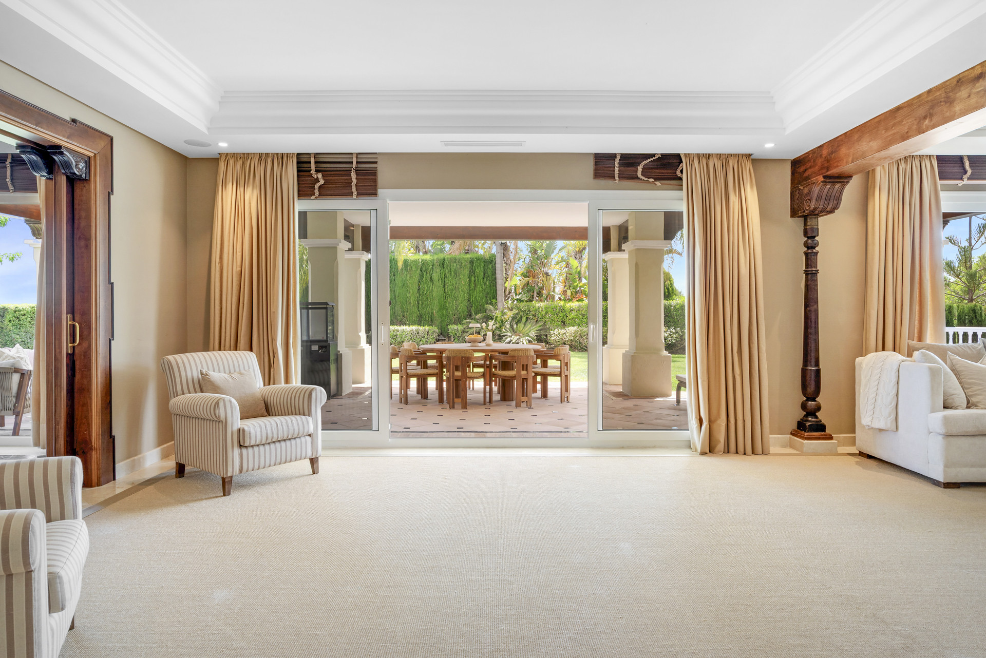 Living room with large windows, two armchairs, and a dining area visible outside.