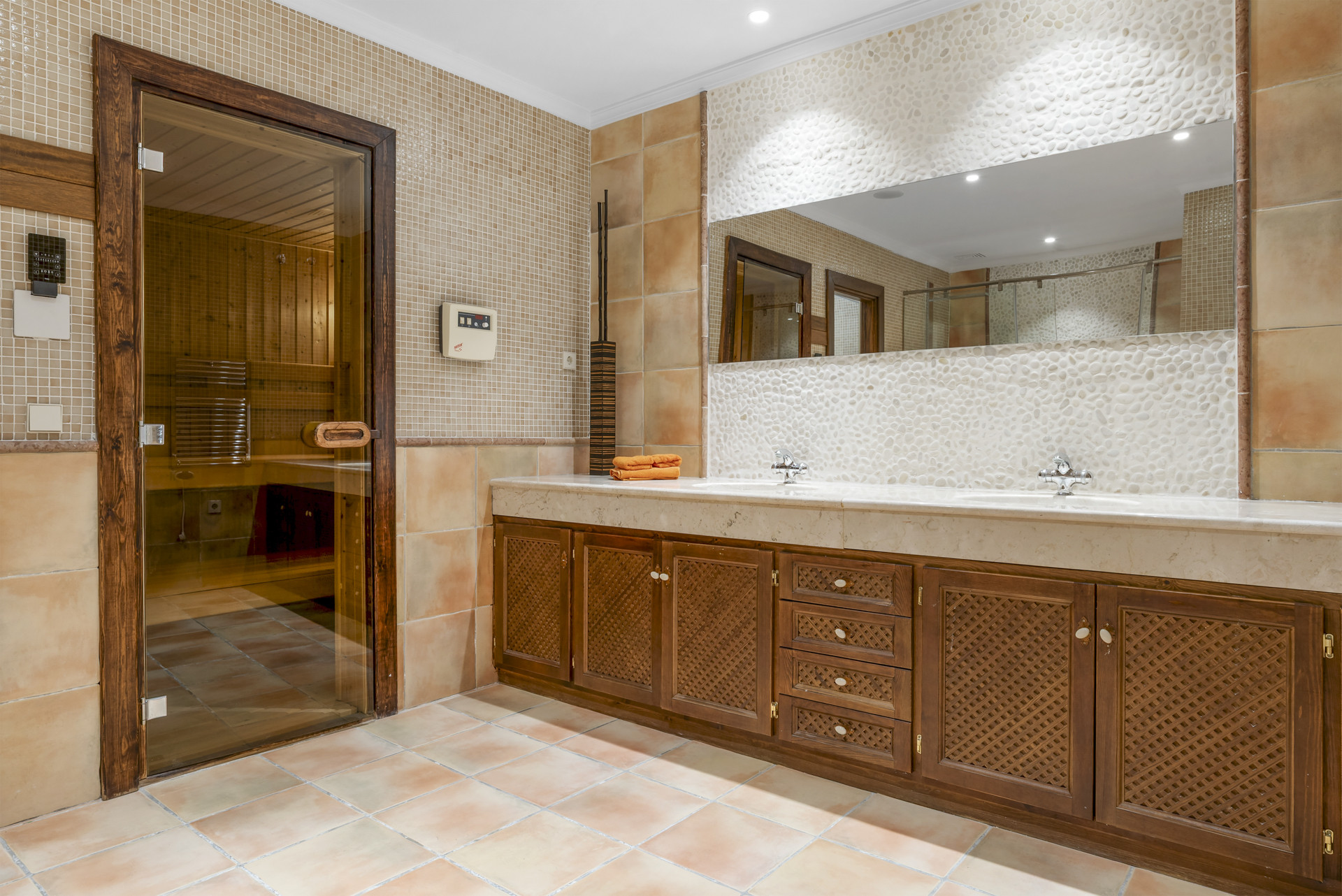 Spacious bathroom with dual sinks, stone tiles, and a visible sauna entrance.