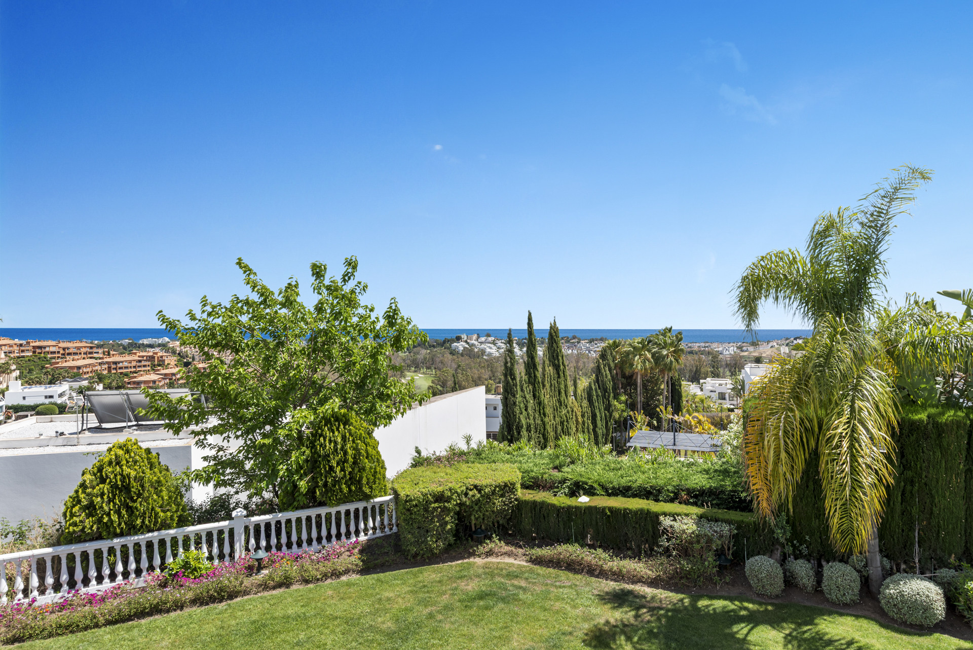 Lush garden with manicured hedges and sea views beneath a clear blue sky.