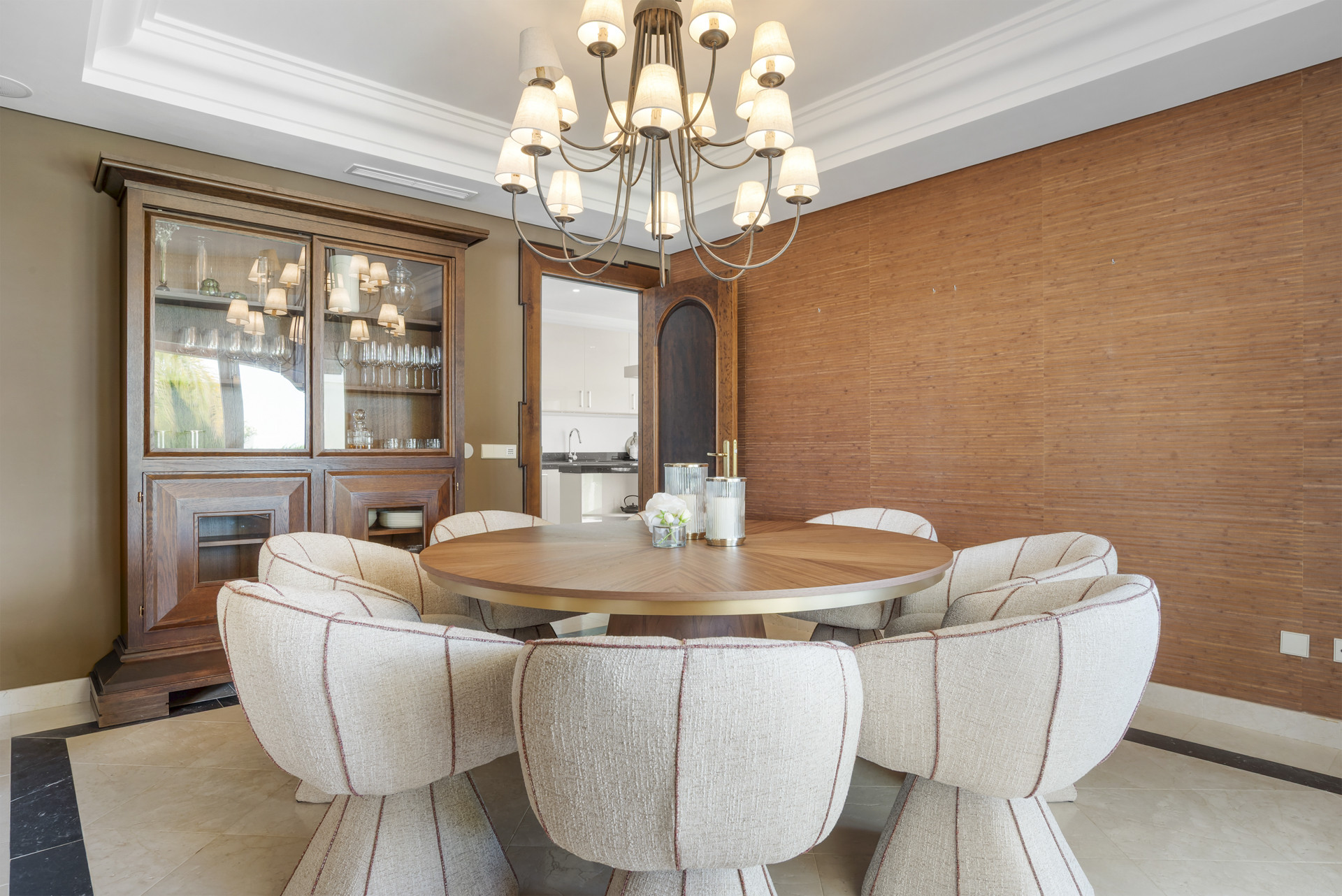Dining room featuring round table, plush chairs, and a glass display cabinet in the background.