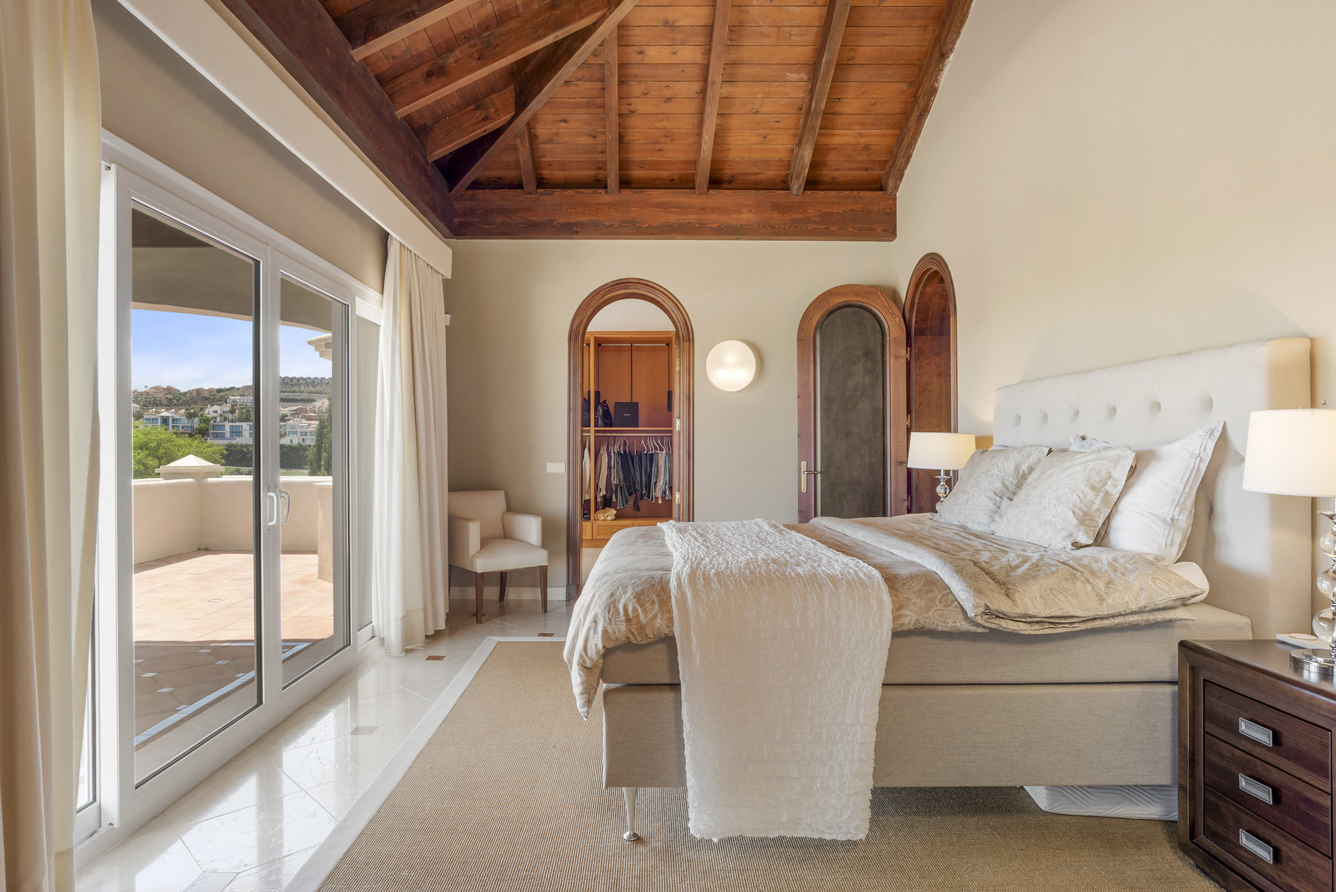Another bedroom with a large window, light-toned furnishings, and an open closet area.