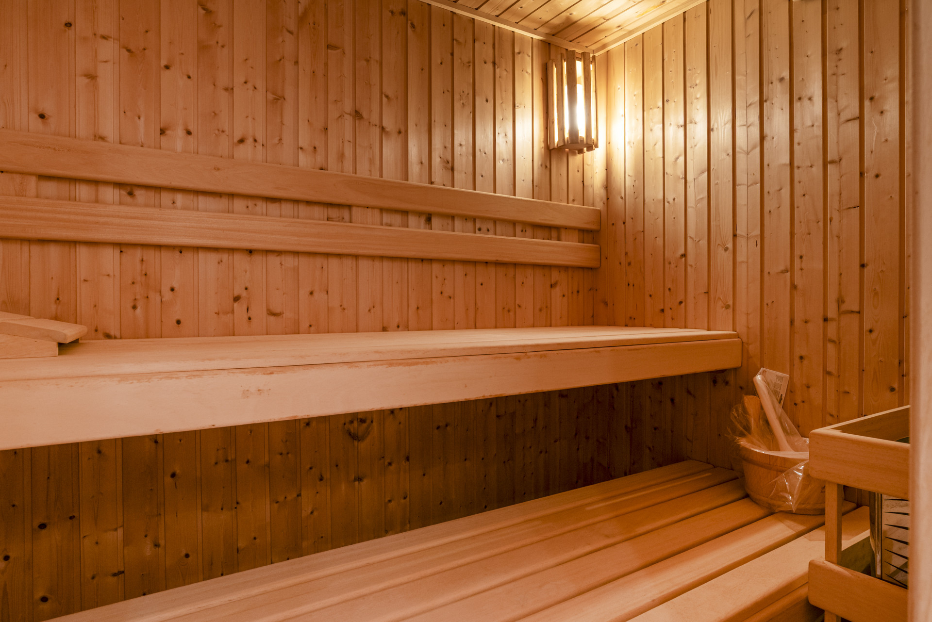 Wood-panelled sauna with benches and a soft light fixture.