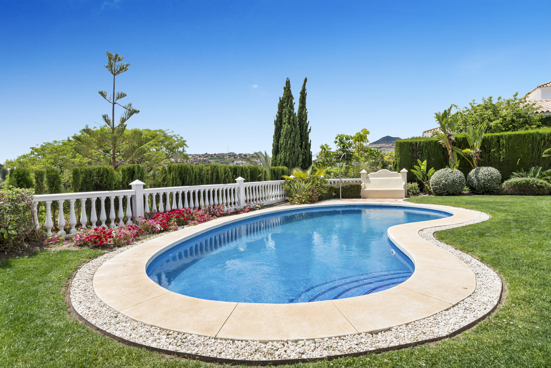 Swimming pool surrounded by garden beds and lush green landscaping.