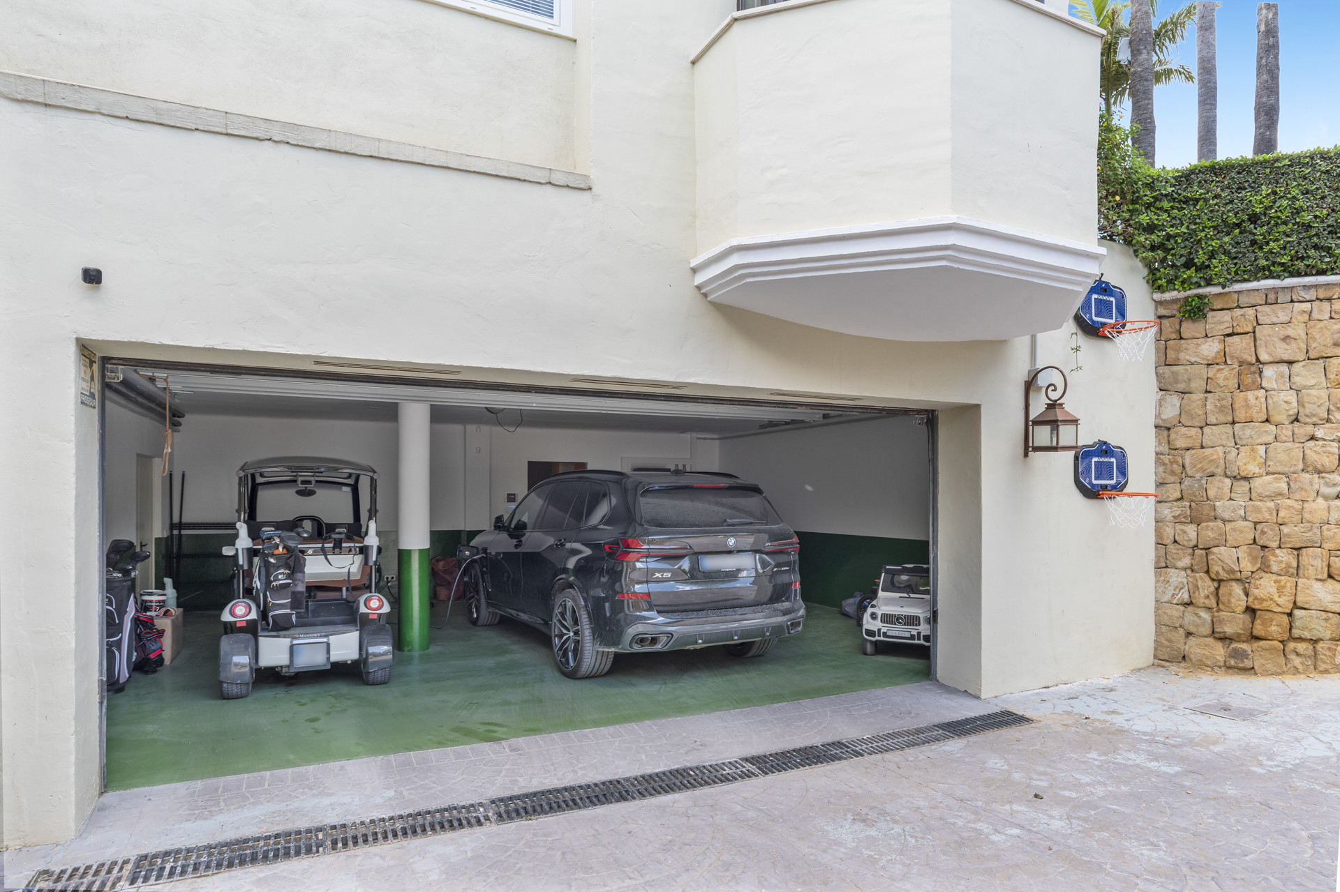 Garage showcasing multiple vehicles with a green floor and stone wall outside.