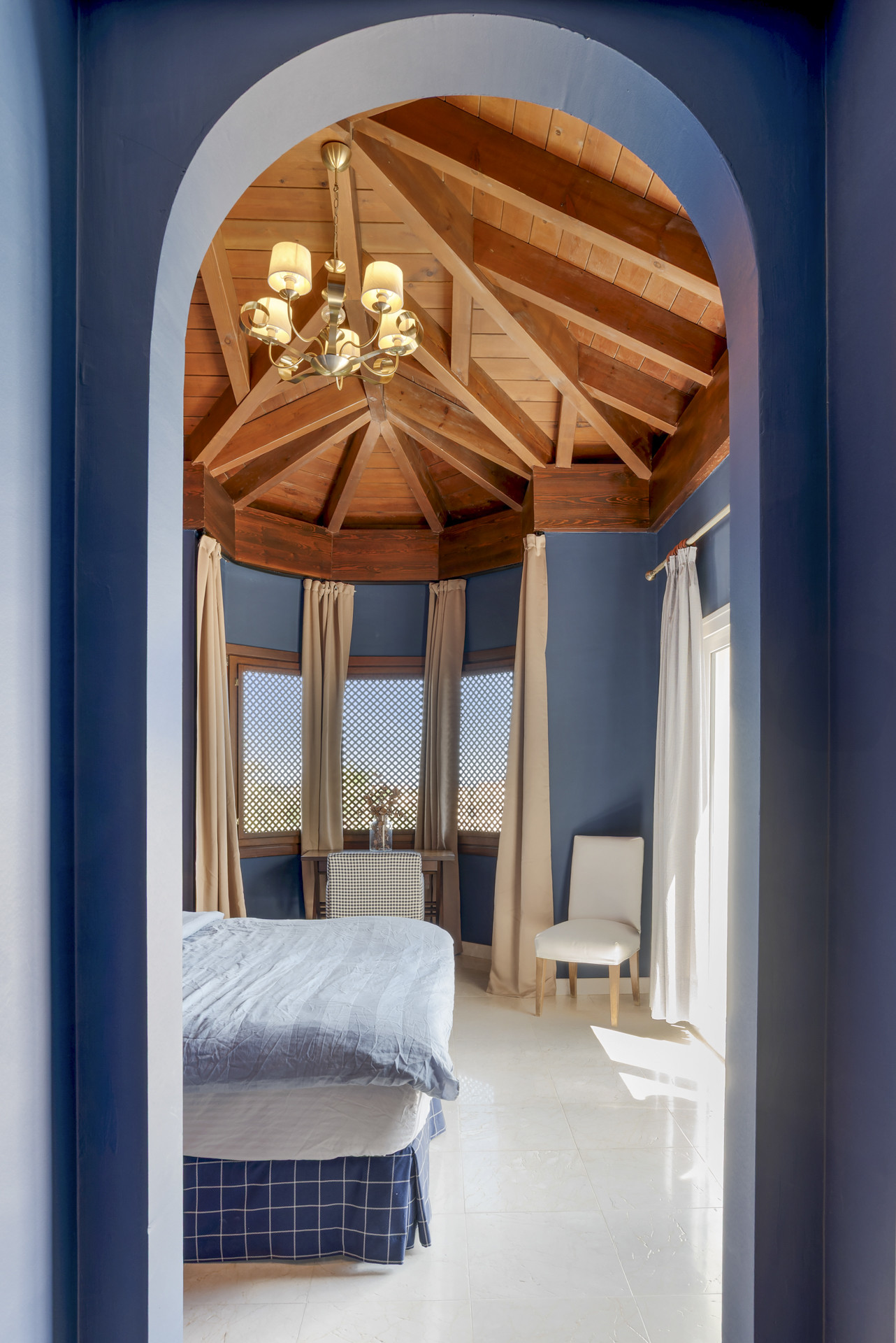 Bedroom featuring a high ceiling, wood beams, and a cozy chair near the window.