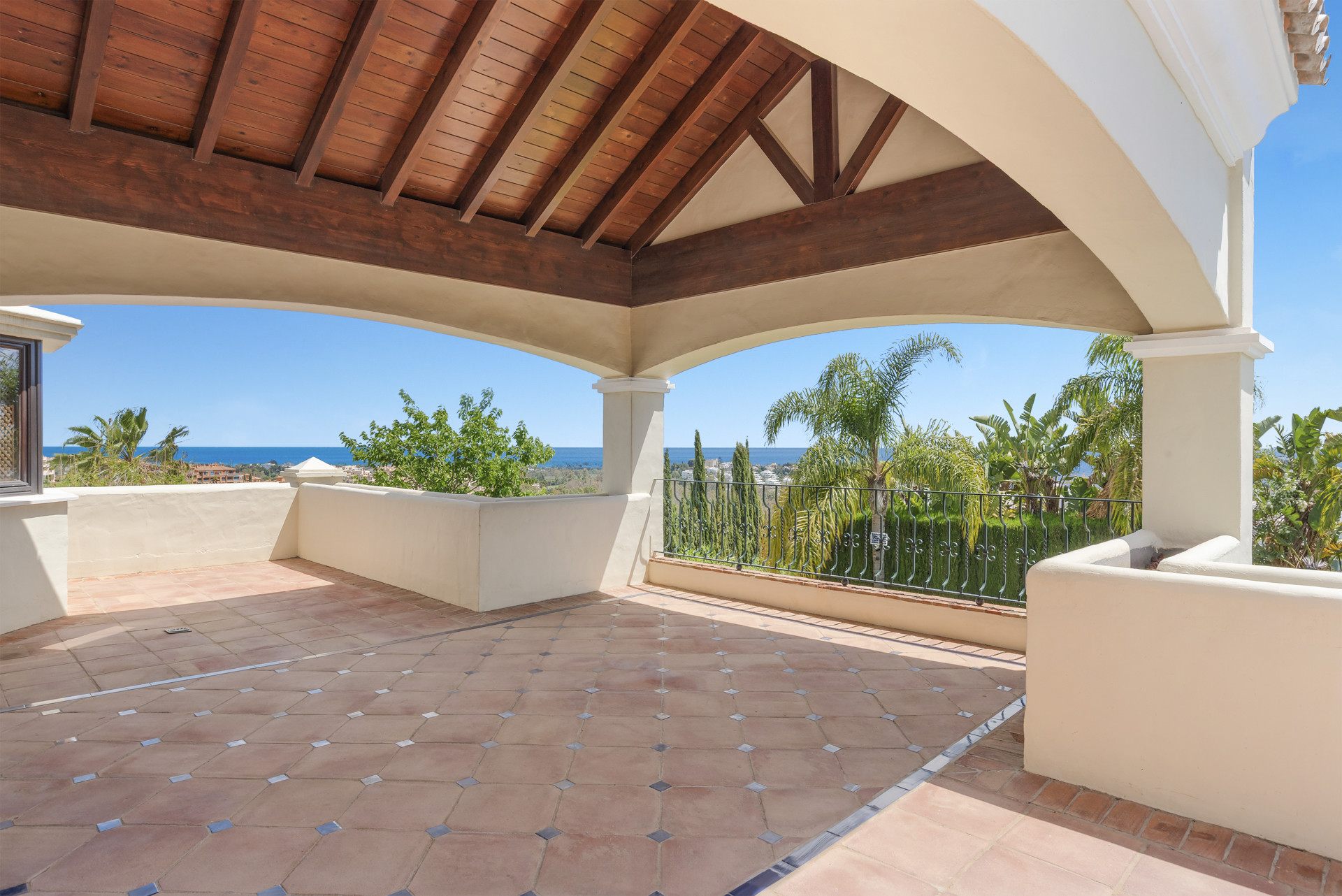 Covered terrace with wooden beams and tiles overlooking views of palm trees and the ocean.
