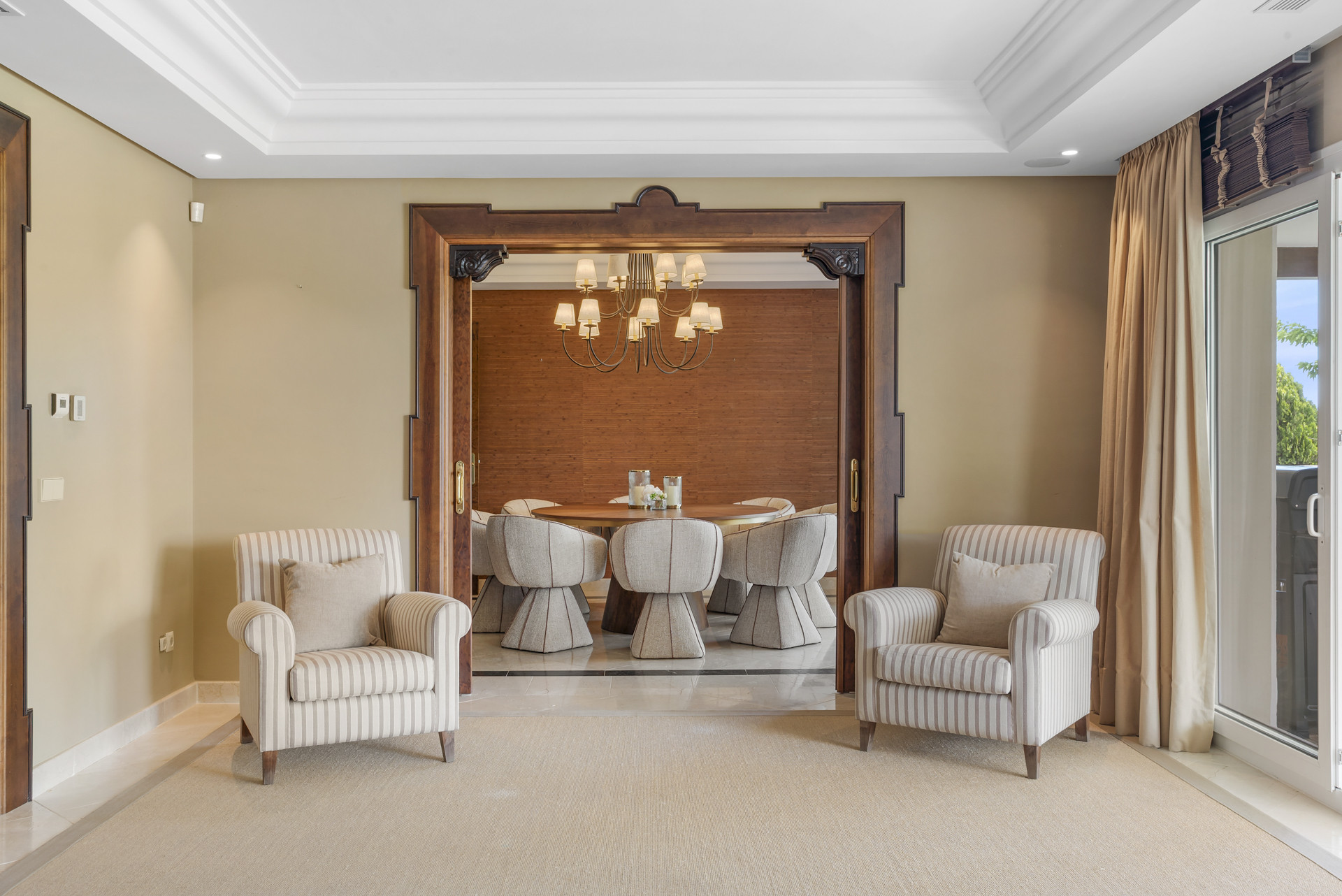 Seating area with two striped chairs framed by a doorway leading to a dining room.