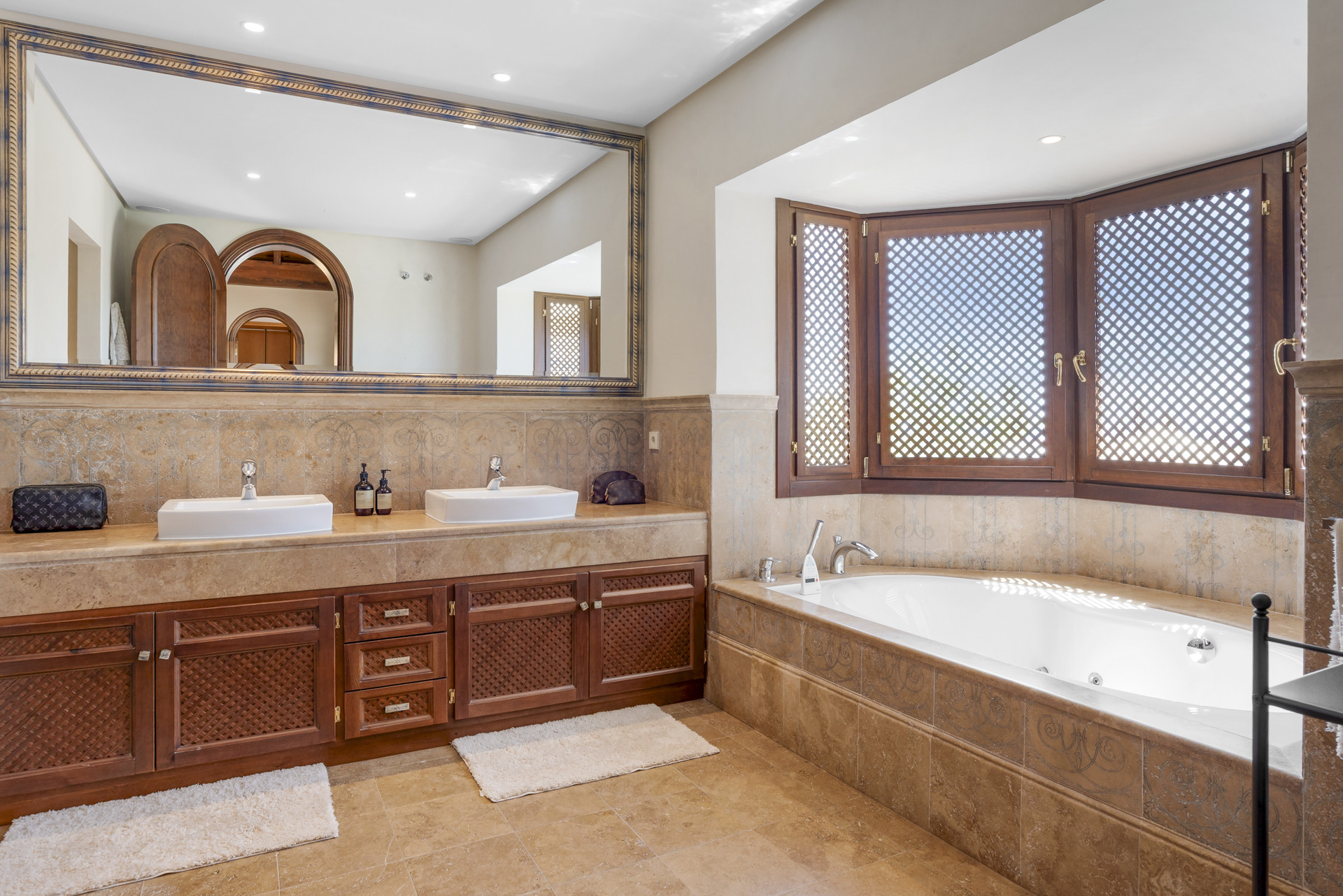 Spacious bathroom featuring dual sinks, a bathtub, and decorative wooden shutters on the window.