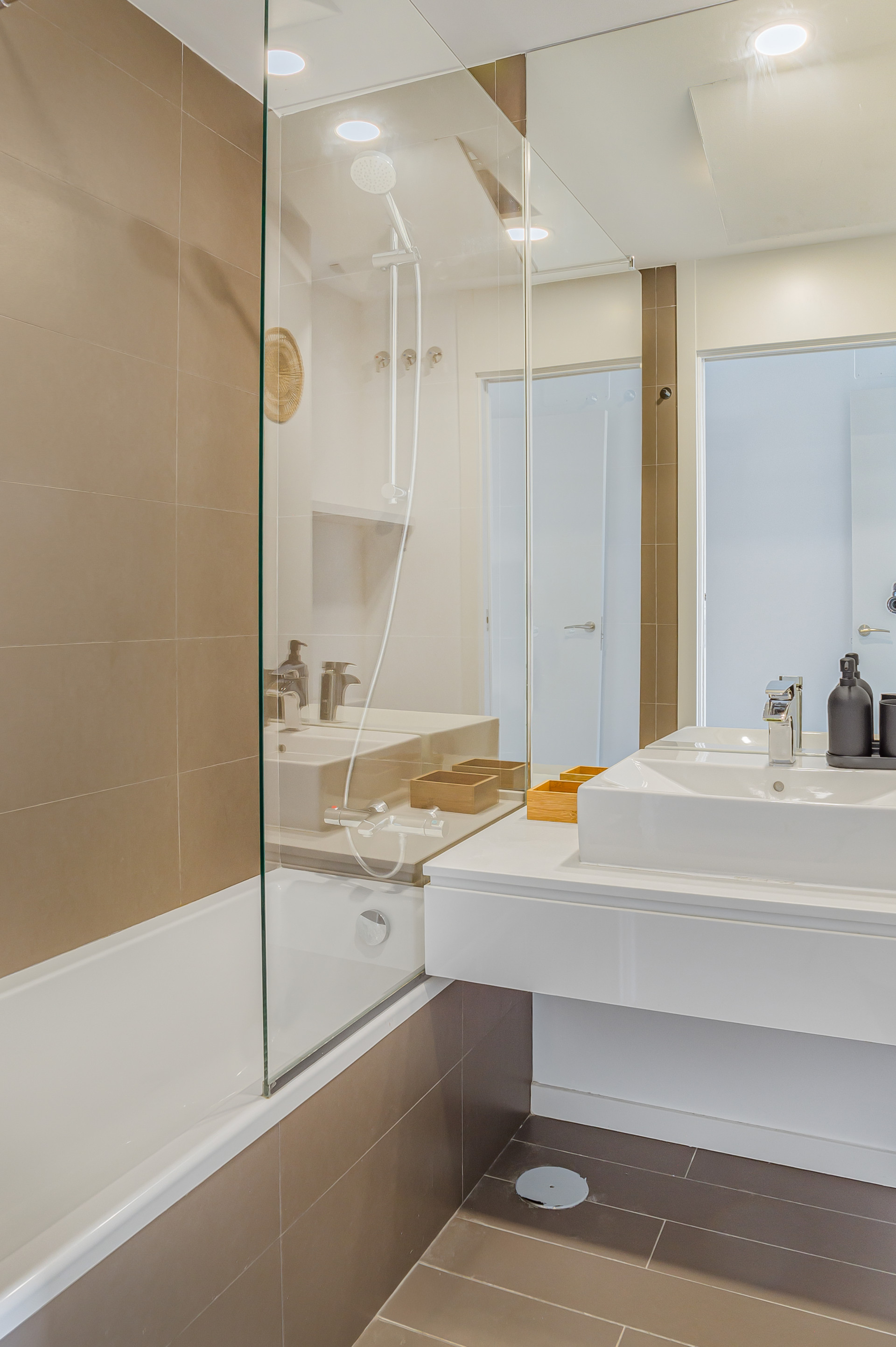Bathroom showing a white bathtub with glass partition, vanity, sink, and tiled floor.