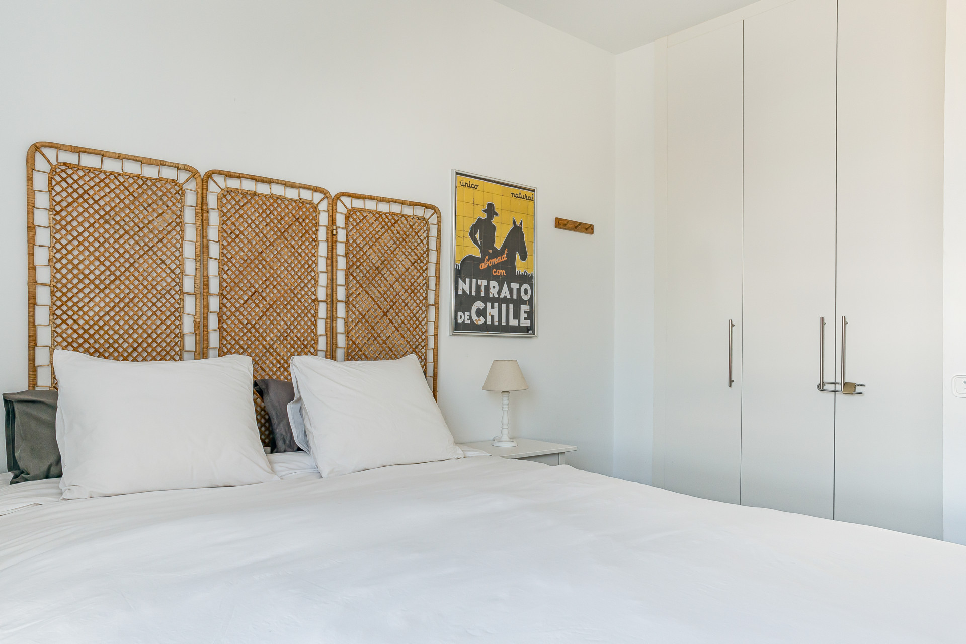 Bedroom with a wicker headboard, white bedding, nightstand lamp, and built-in closet.