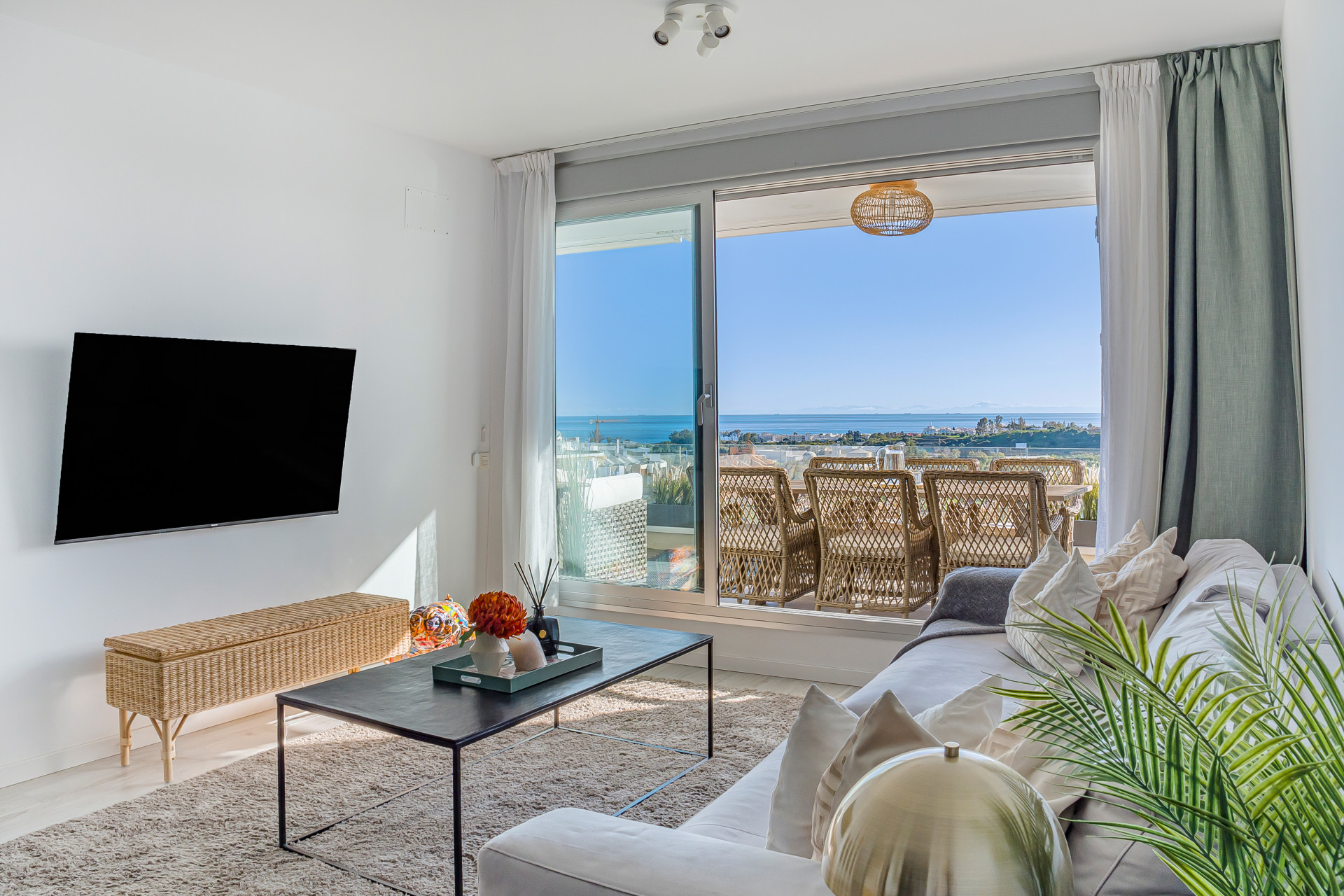 Living room with white sofa, TV, coffee table, and sliding glass doors to a balcony with sea views.