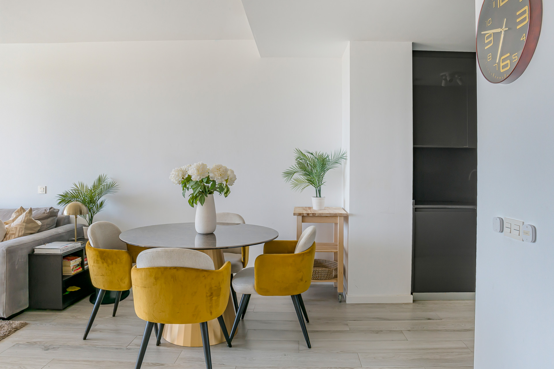 Dining area with a round table and yellow chairs, green plants, and a partial view of kitchen cabinetry.