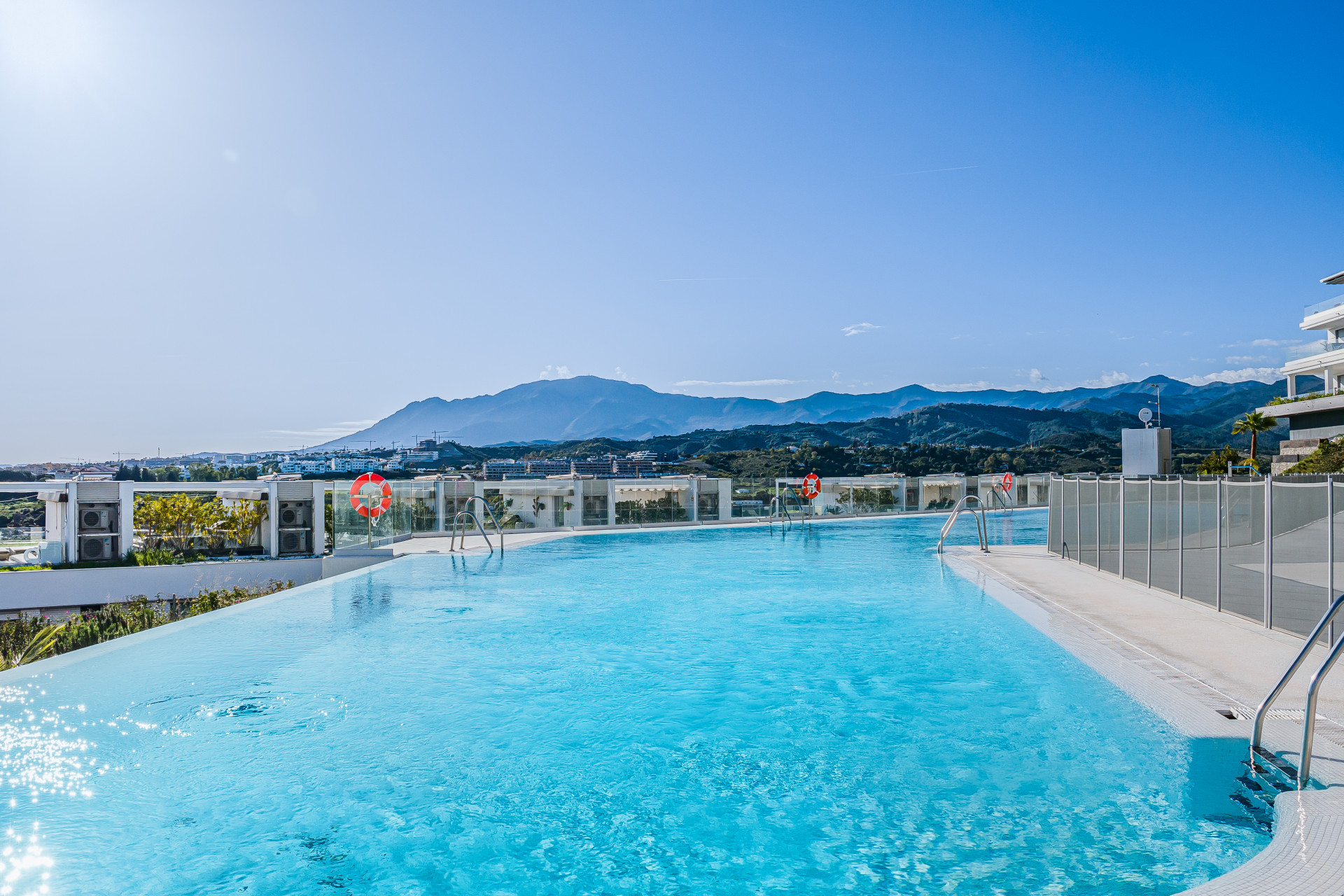 Infinity pool with bright blue water and mountainous landscape in the distance under clear sky.