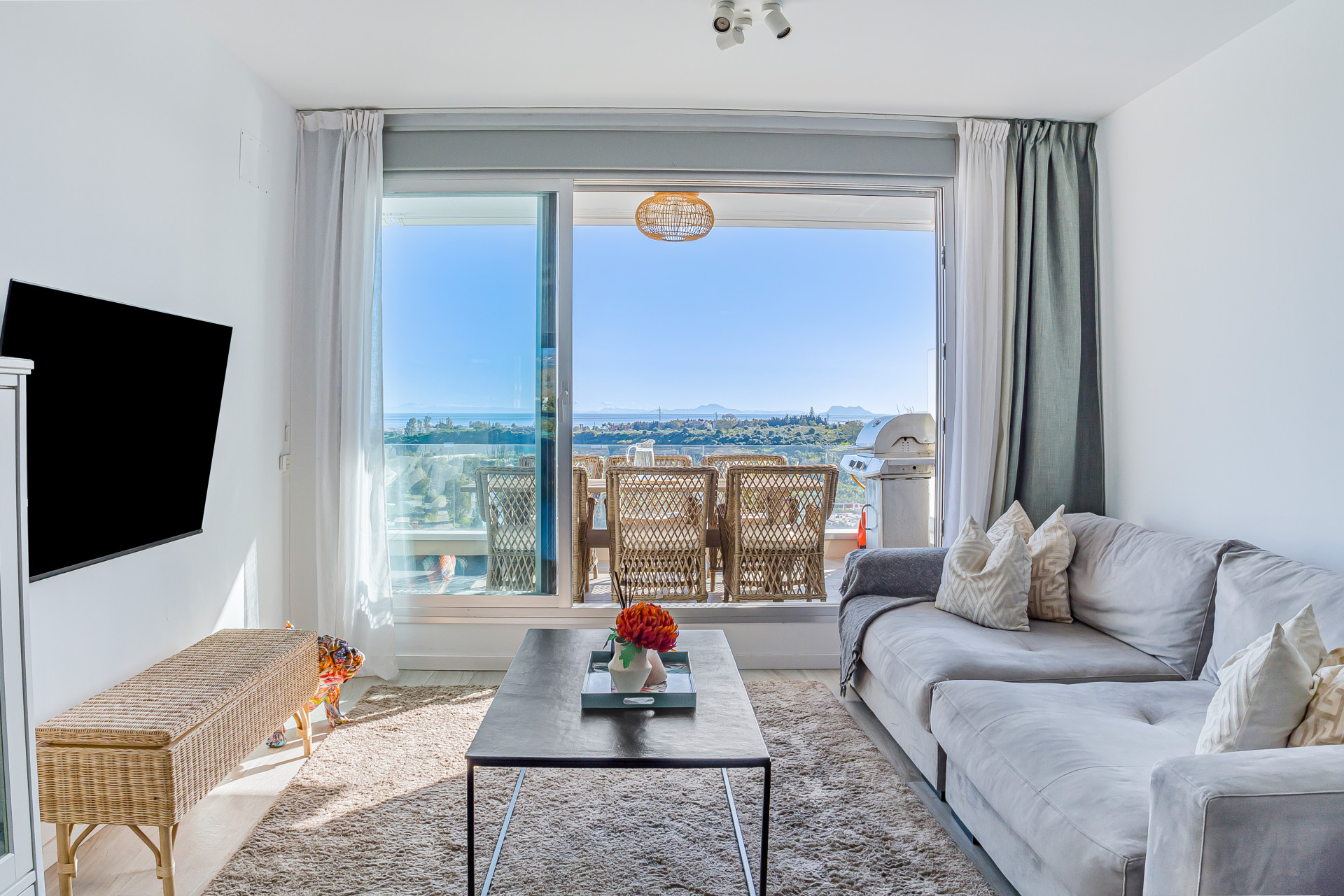 Living room with gray sectional sofa, coffee table, TV, and large glass doors opening to an outdoor balcony.
