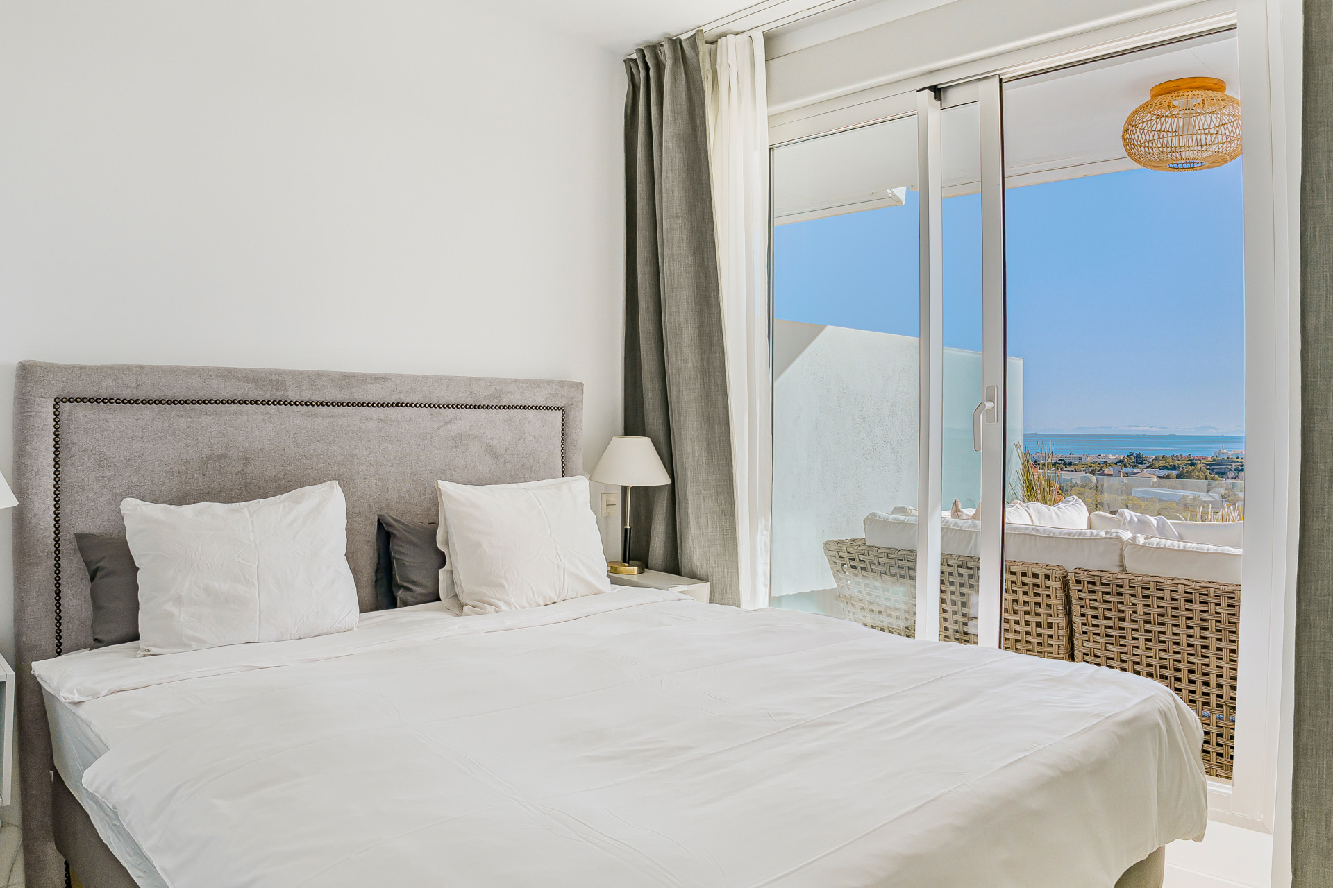 Bedroom with a large bed, gray headboard, and sliding glass doors to a balcony with sea views.