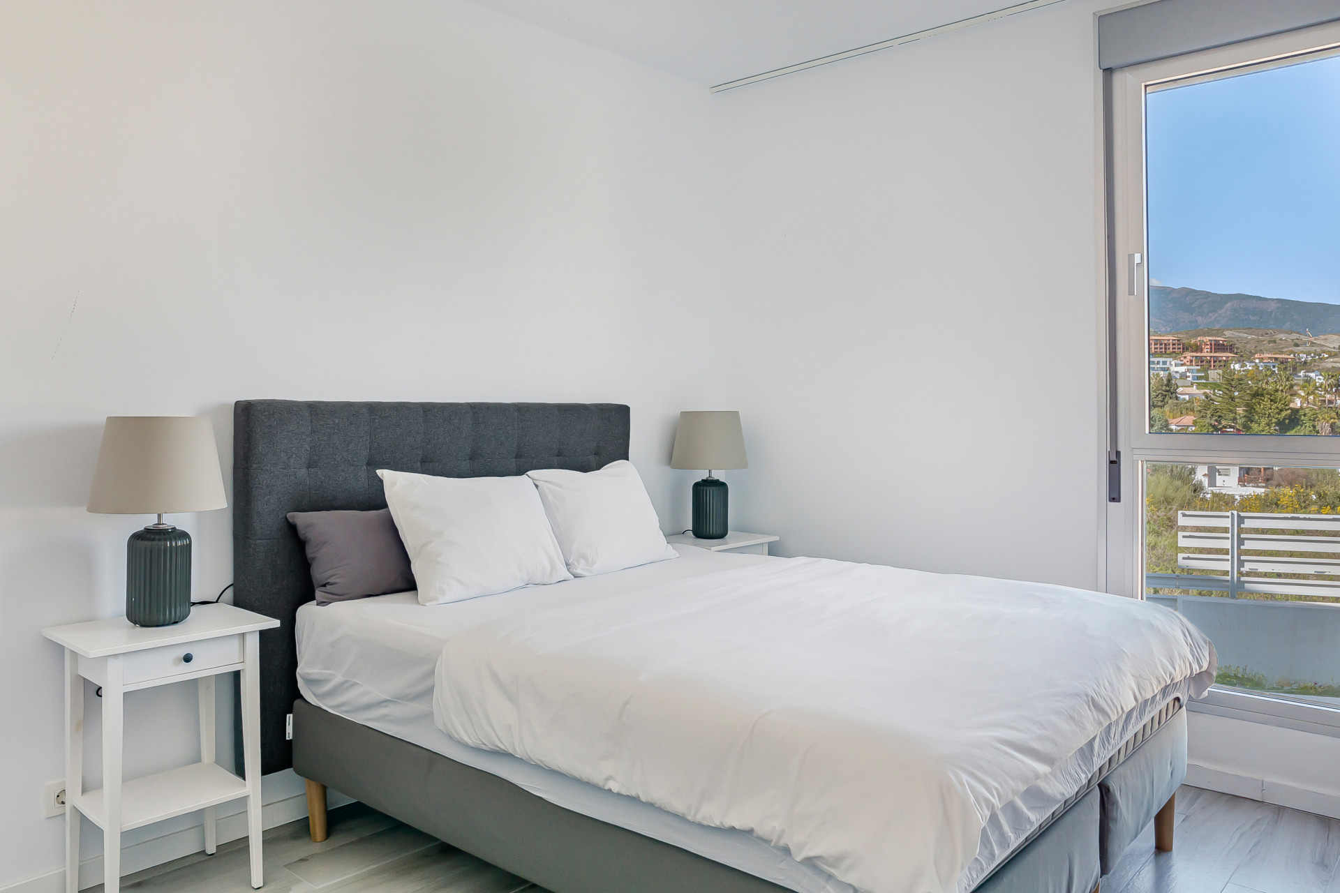 Bedroom with a large window offering mountain views, a bed with gray headboard, and two bedside tables.