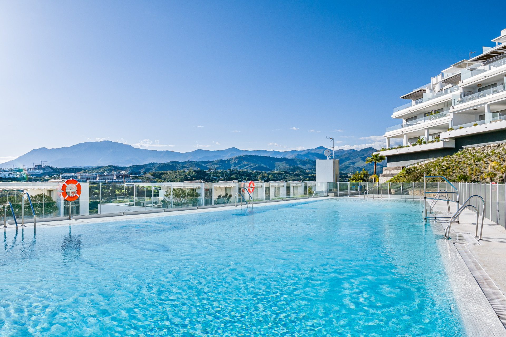 Outdoor infinity pool overlooking mountains and distant buildings under a clear blue sky.