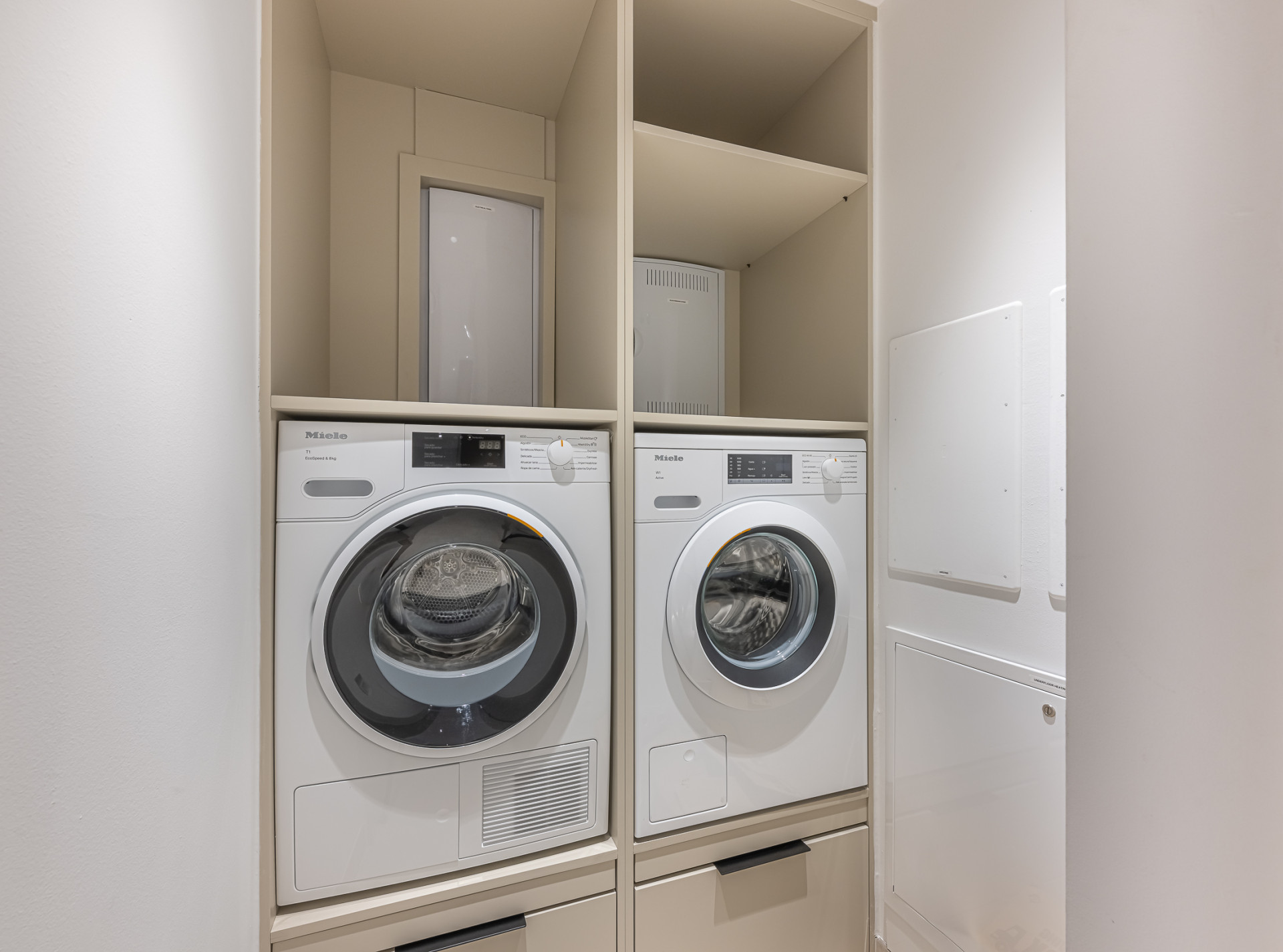 Laundry room with stacked white Miele washer and dryer units built into light wood cabinetry.