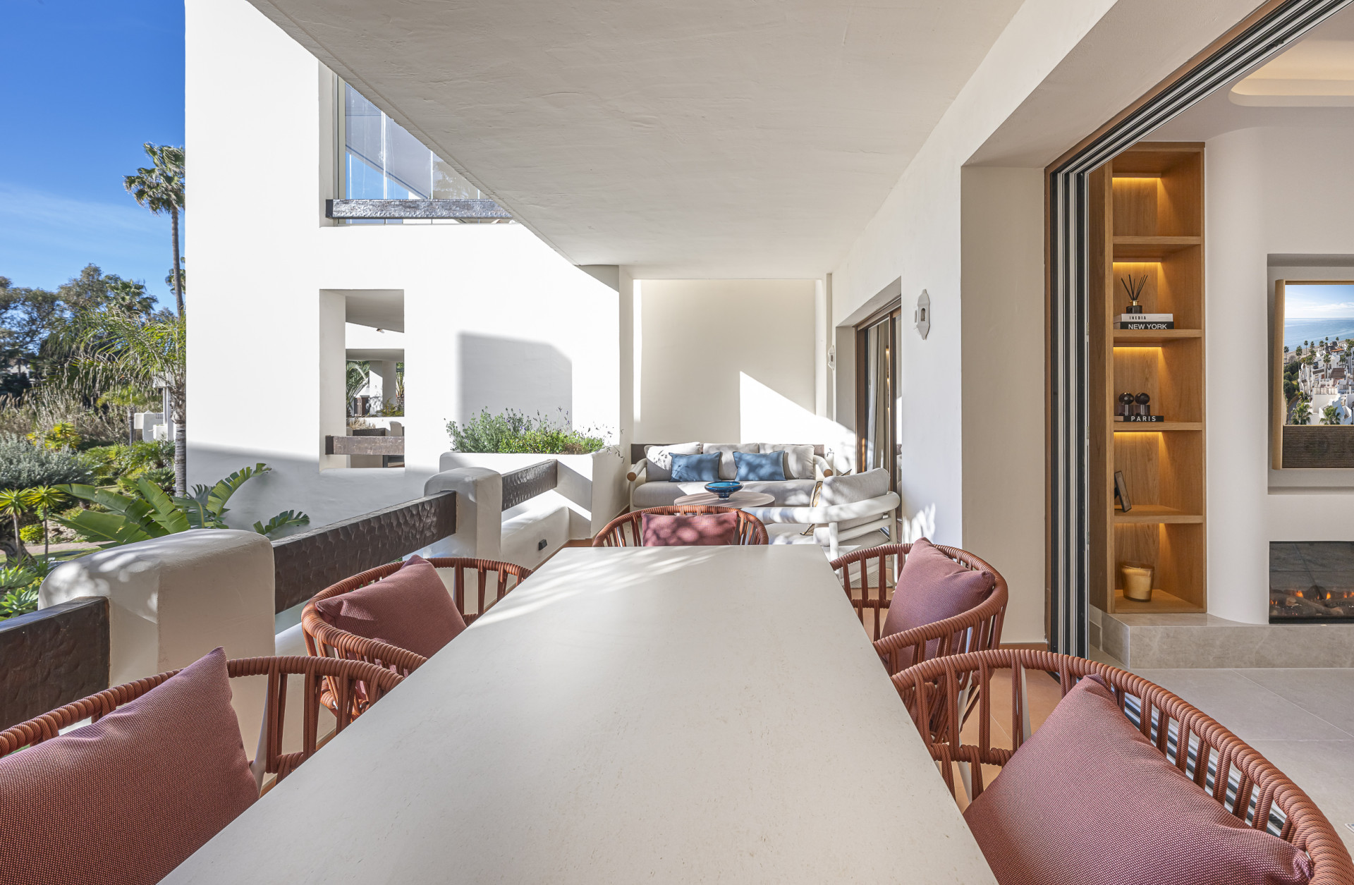 Covered balcony with a long dining table, seating area, and built-in shelving unit with decor.
