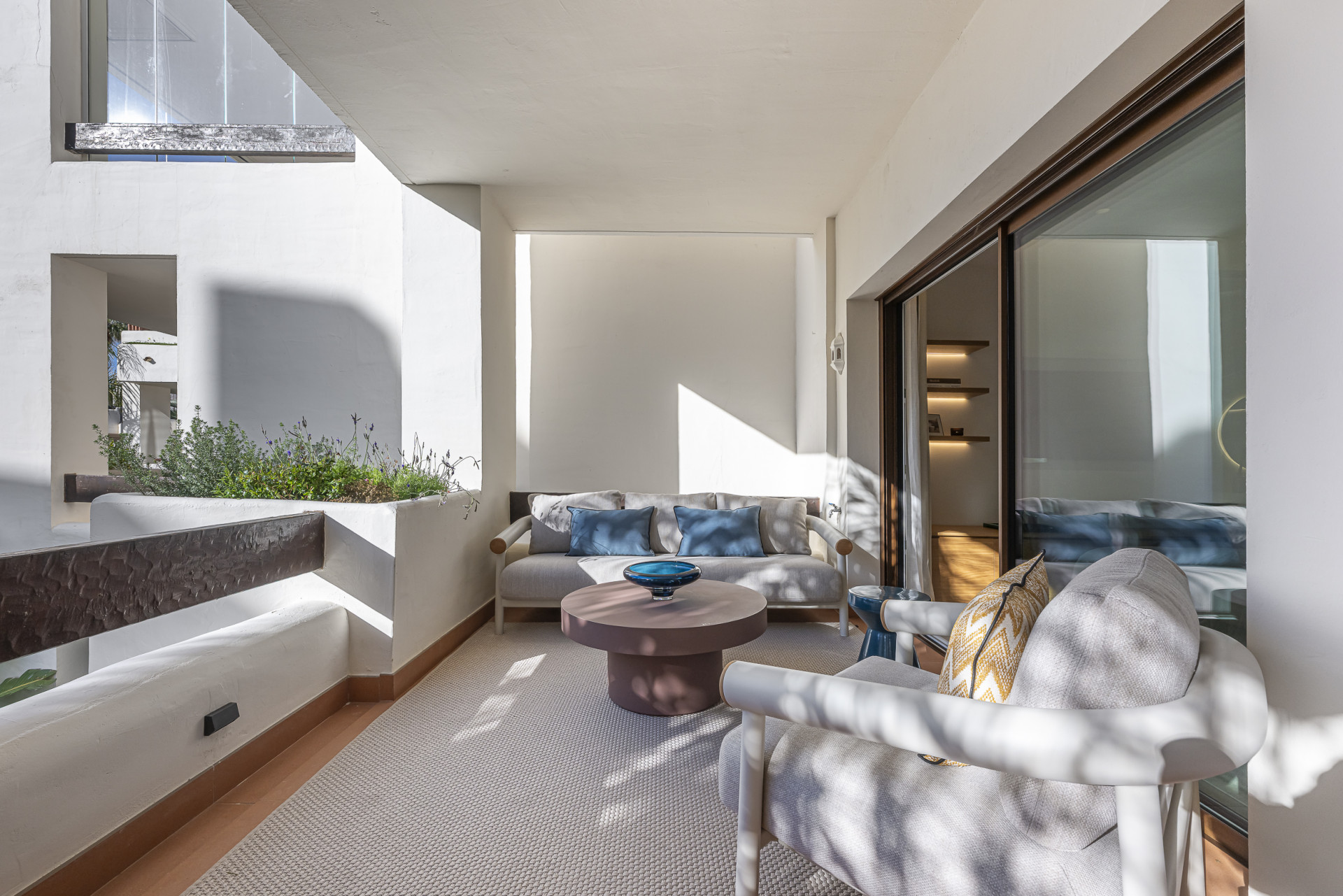 Covered balcony with a cream rug, outdoor sofa, armchair, and sliding glass door entrance.