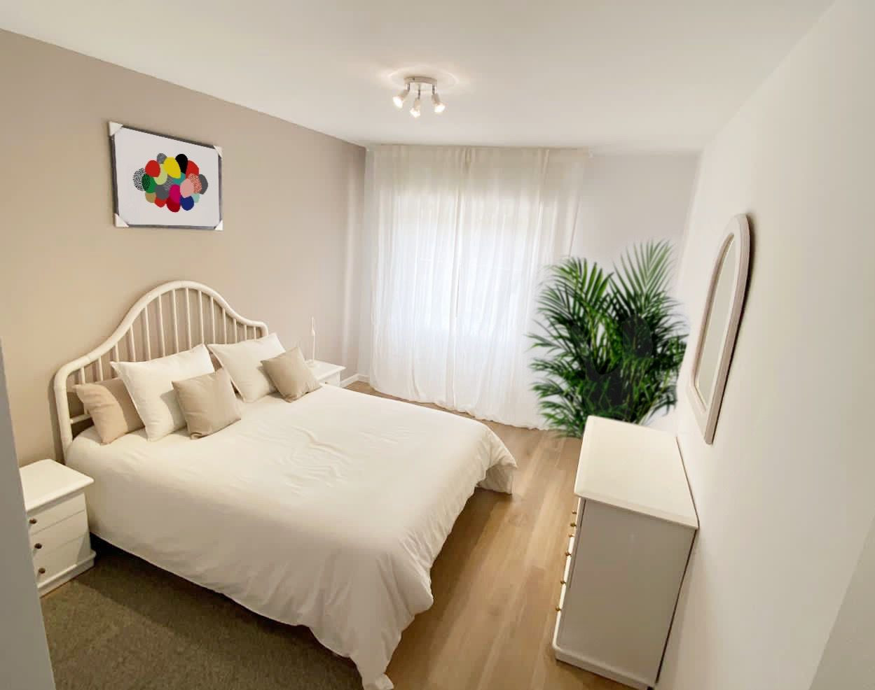 Bedroom with light wood floor, white bed, nightstands, dresser, sheer curtains, and large green plant.