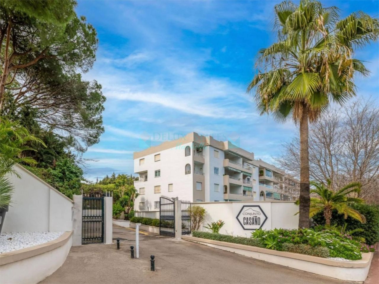 Exterior view of an apartment building entrance with a driveway, black gate, and "Conjunto Casano" sign.