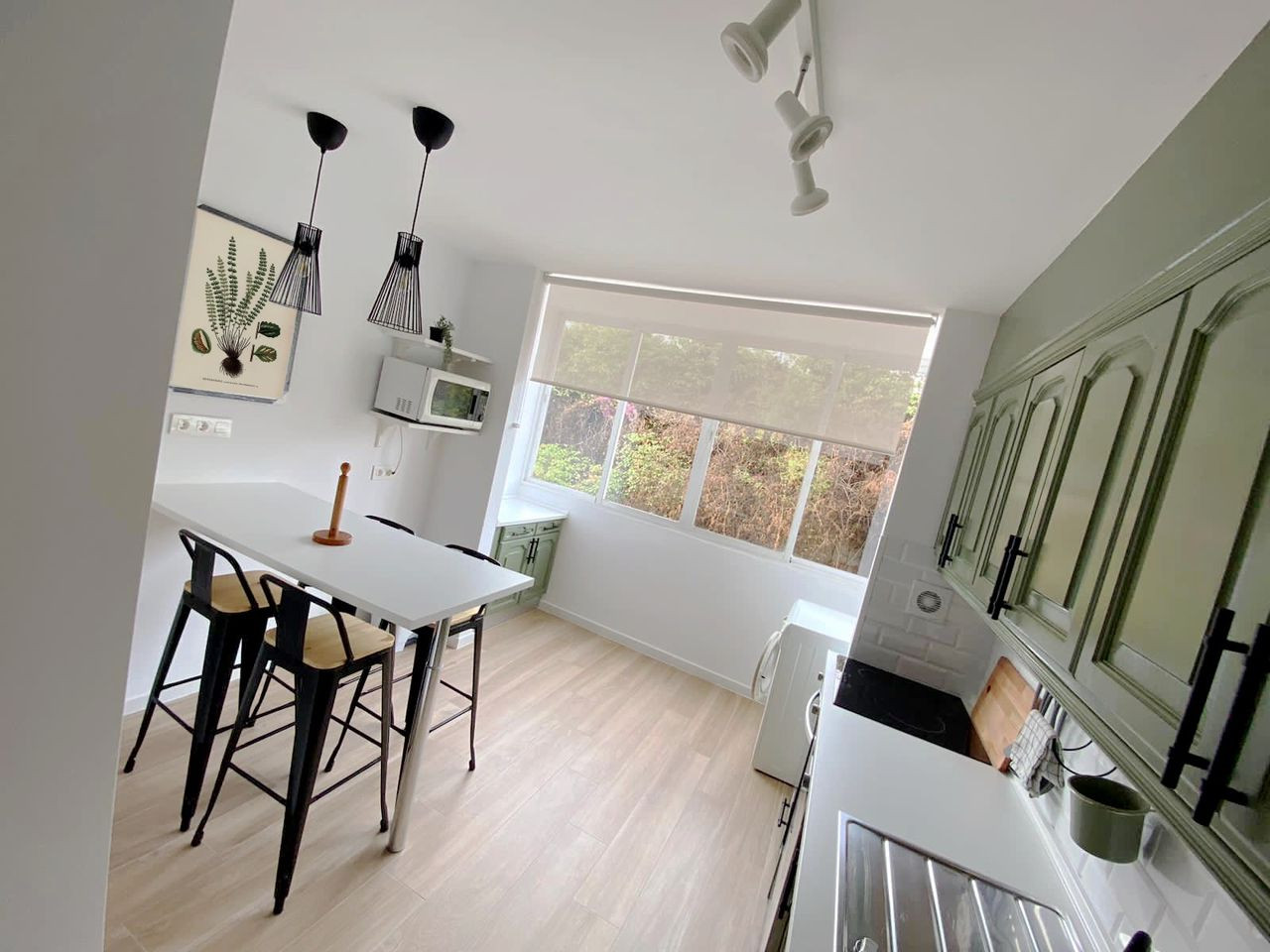 Kitchen view showing a white breakfast bar with two stools, a large window, and green upper cabinets.
