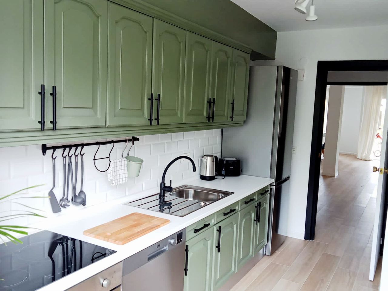 Modern kitchen with olive green upper and lower cabinets, white subway tile, and a stainless steel refrigerator.