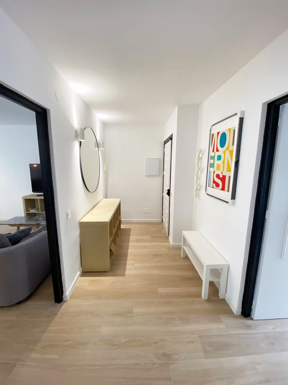 Hallway with a wooden console, round mirror, white bench, and colorful framed art.