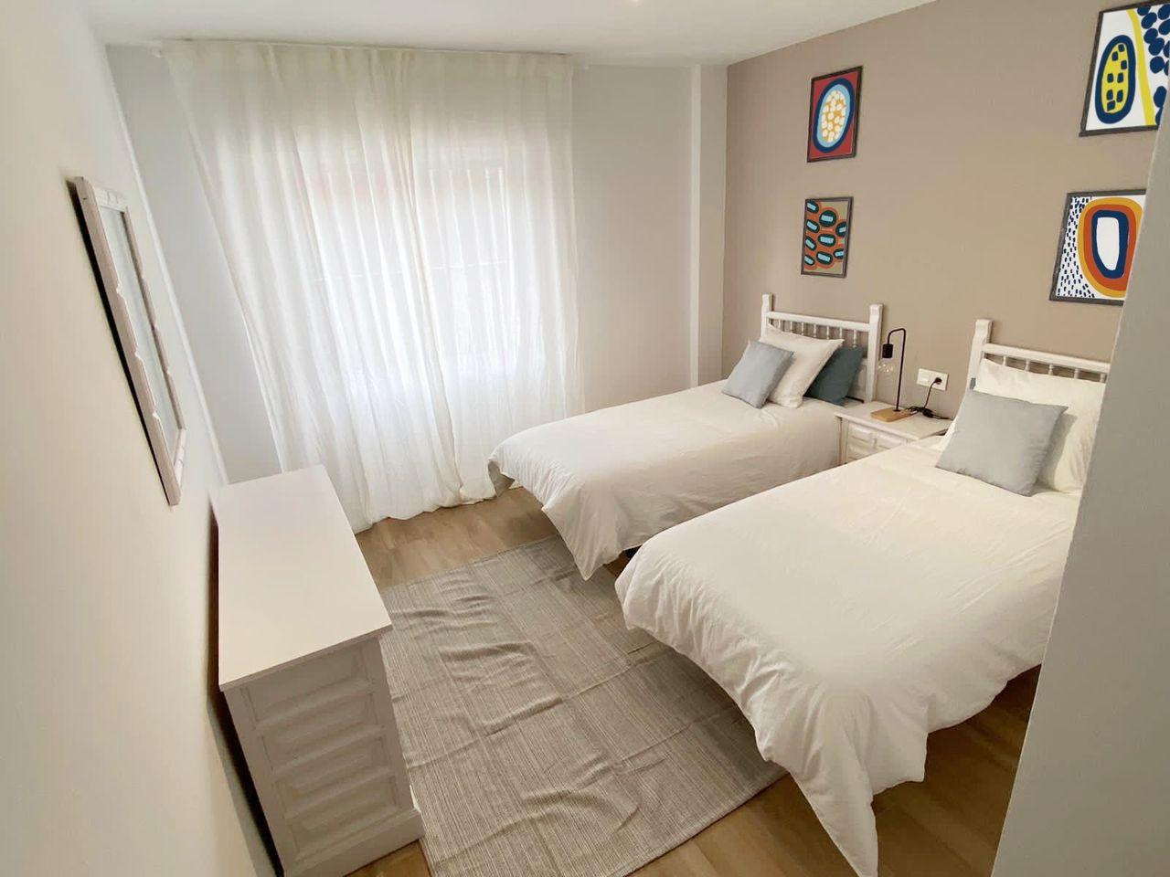 Bedroom with two single beds dressed in white, a white dresser, and vibrant abstract art on the wall.